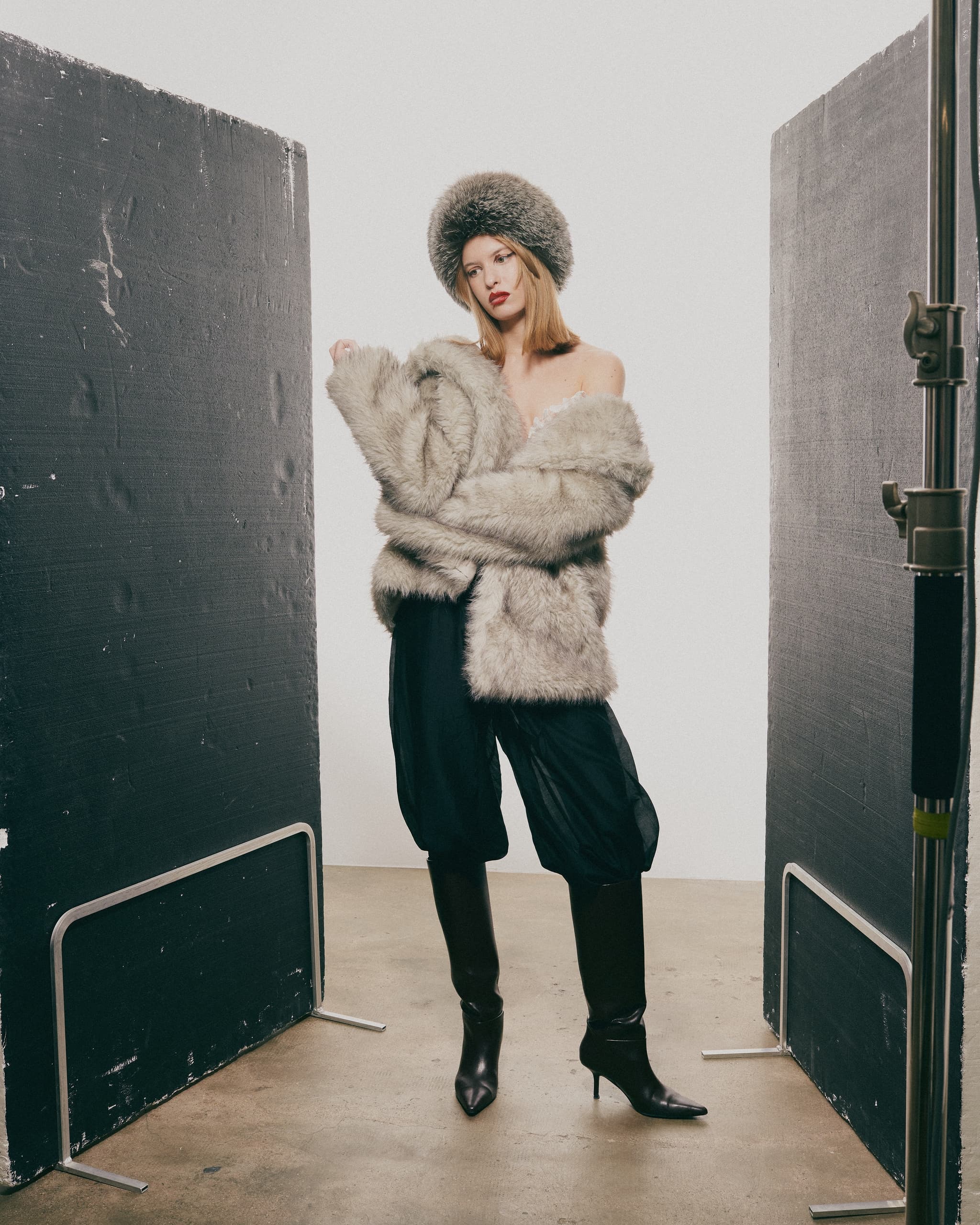 Fashion model in fur coat and hat, posing between studio backdrops.