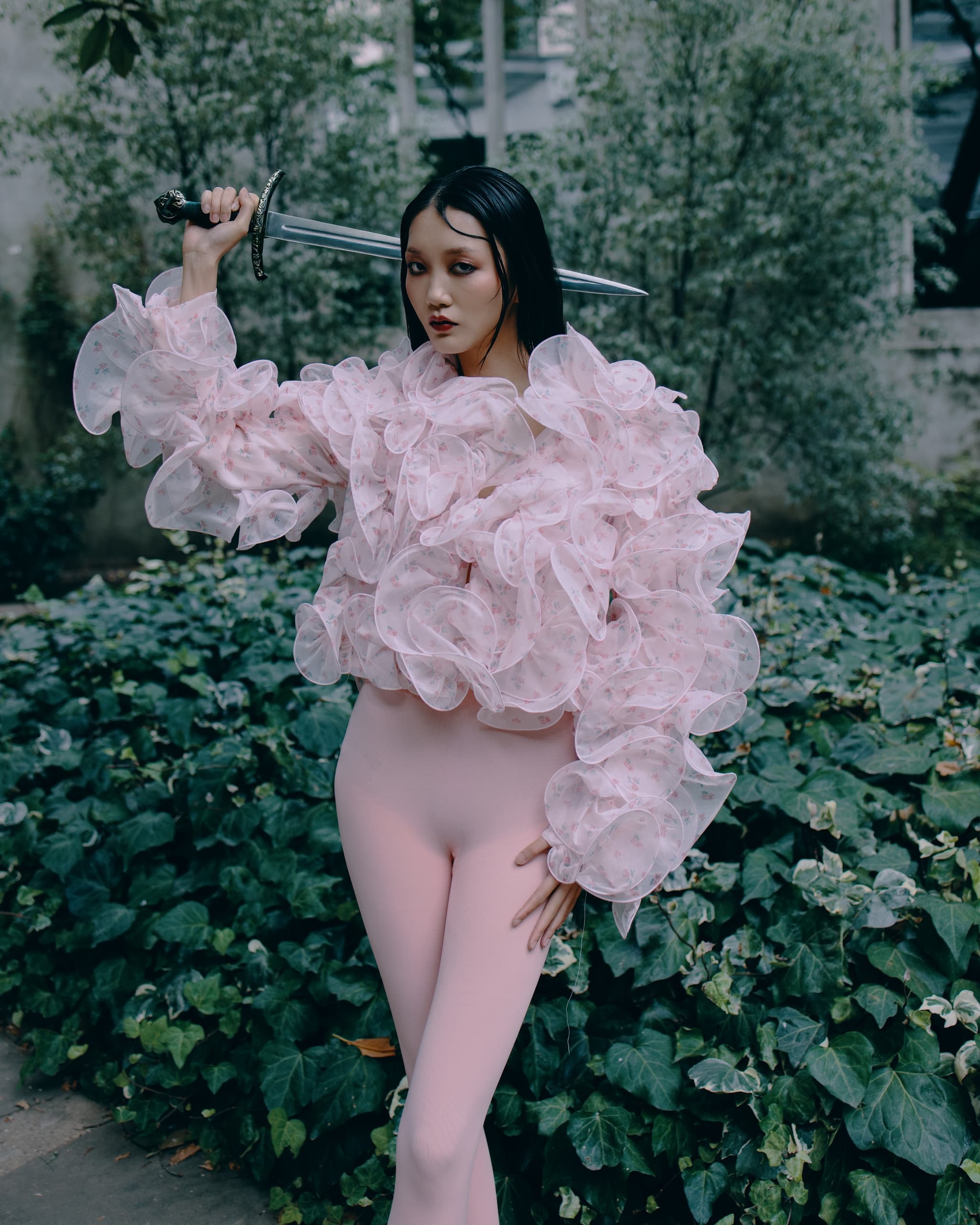 Fashionable warrior in pink ruffled outfit holding a sword, set in lush greenery.