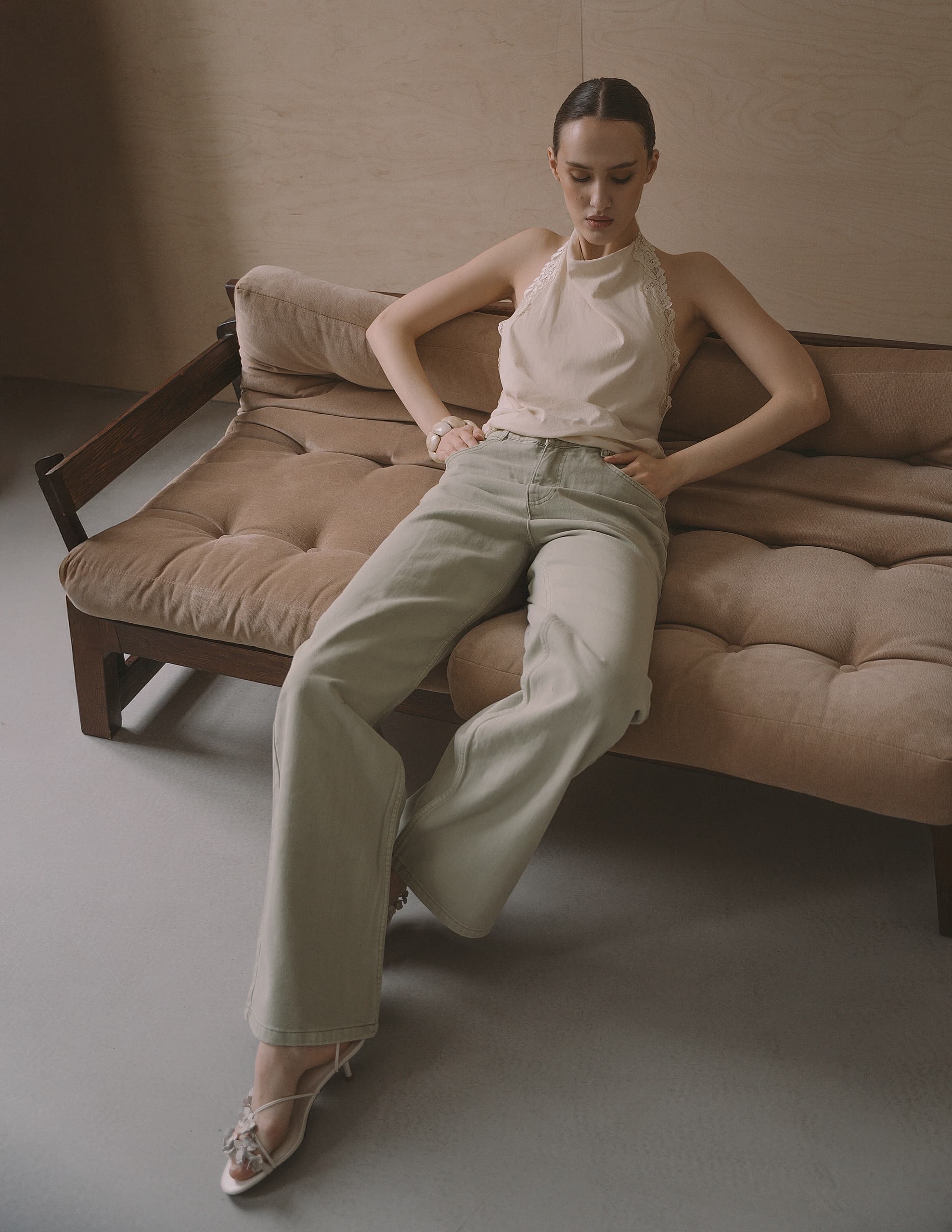Woman in casual outfit sitting on a couch in a minimalist room setting.