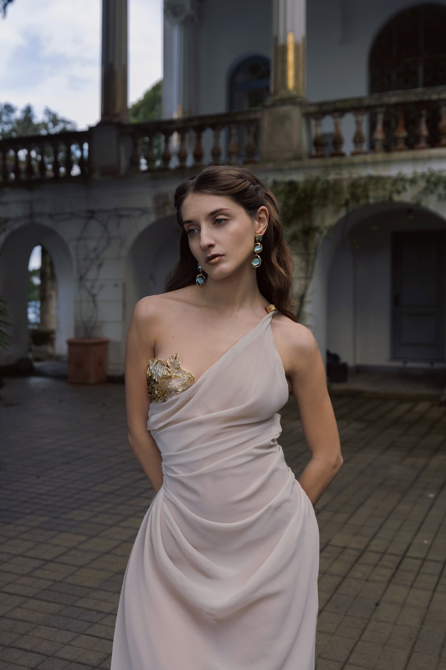 Woman in elegant one-shoulder gown in front of vintage building.