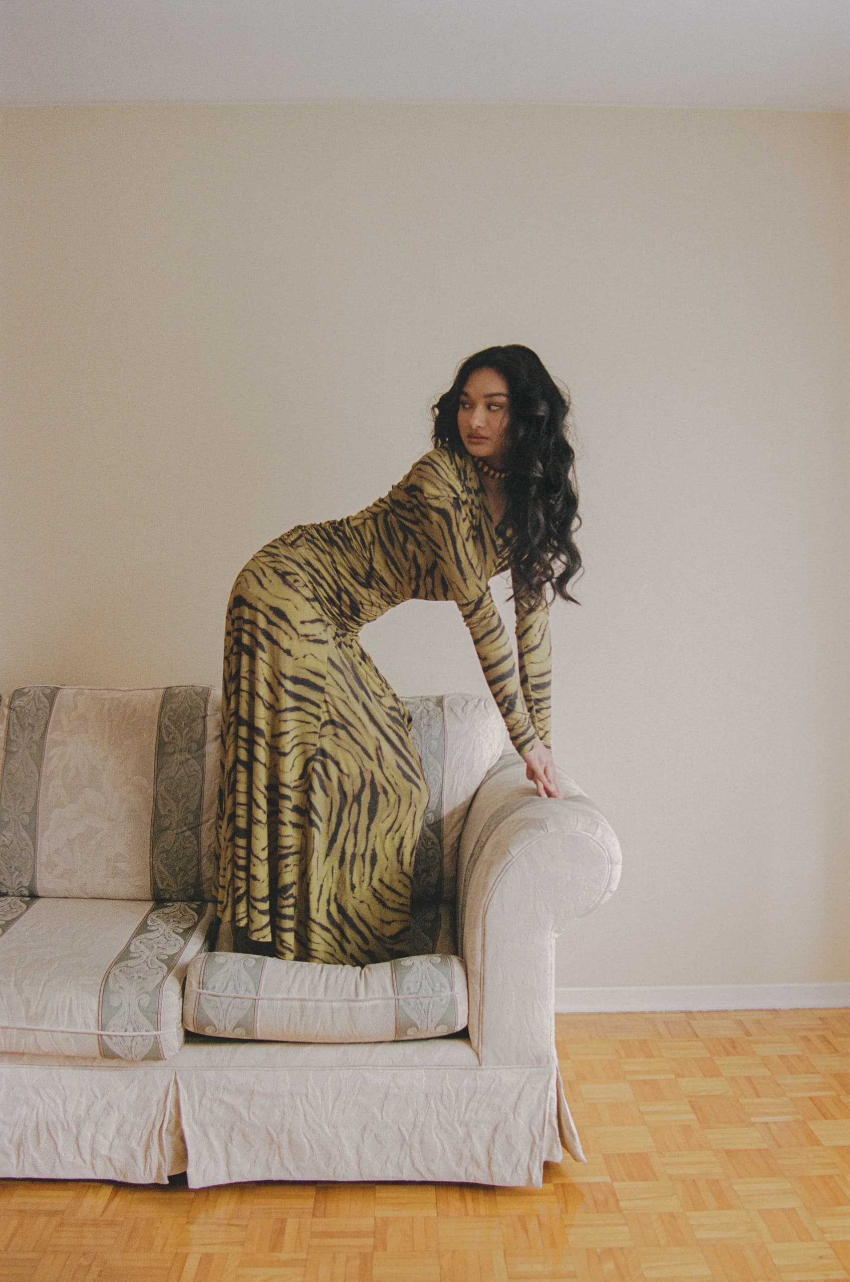 Woman in a tiger-print dress poses on a sofa, exuding style and elegance.