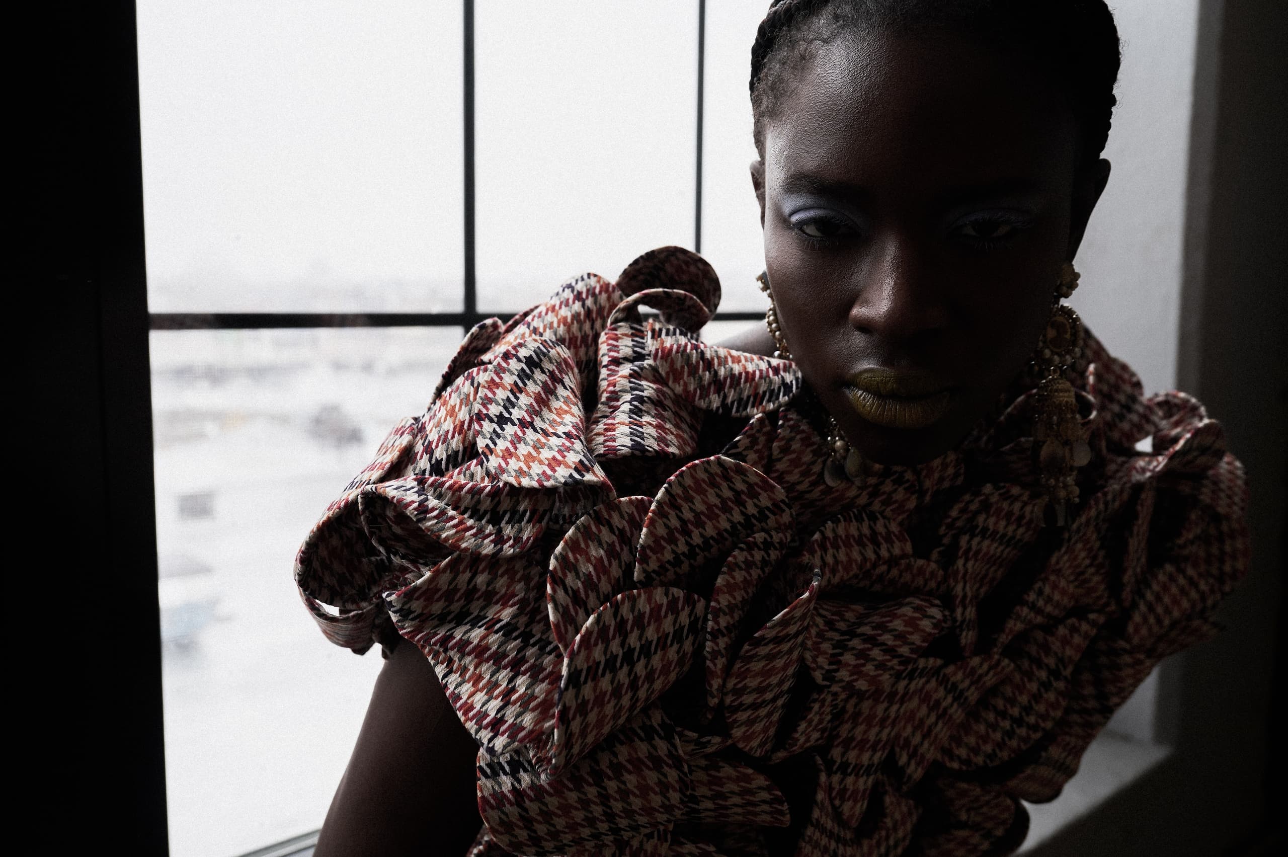 Fashionable person in patterned garment with dramatic lighting by a window.