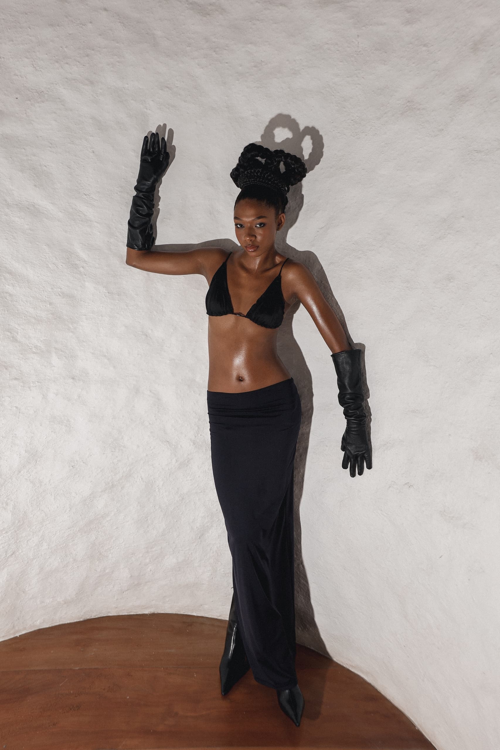 Fashion model poses stylishly in black attire against a textured white background.