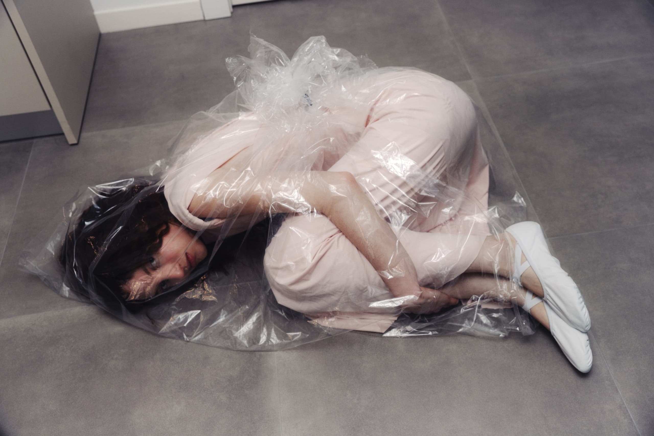 Person wrapped in plastic on the floor, creating a dramatic, artful scene.