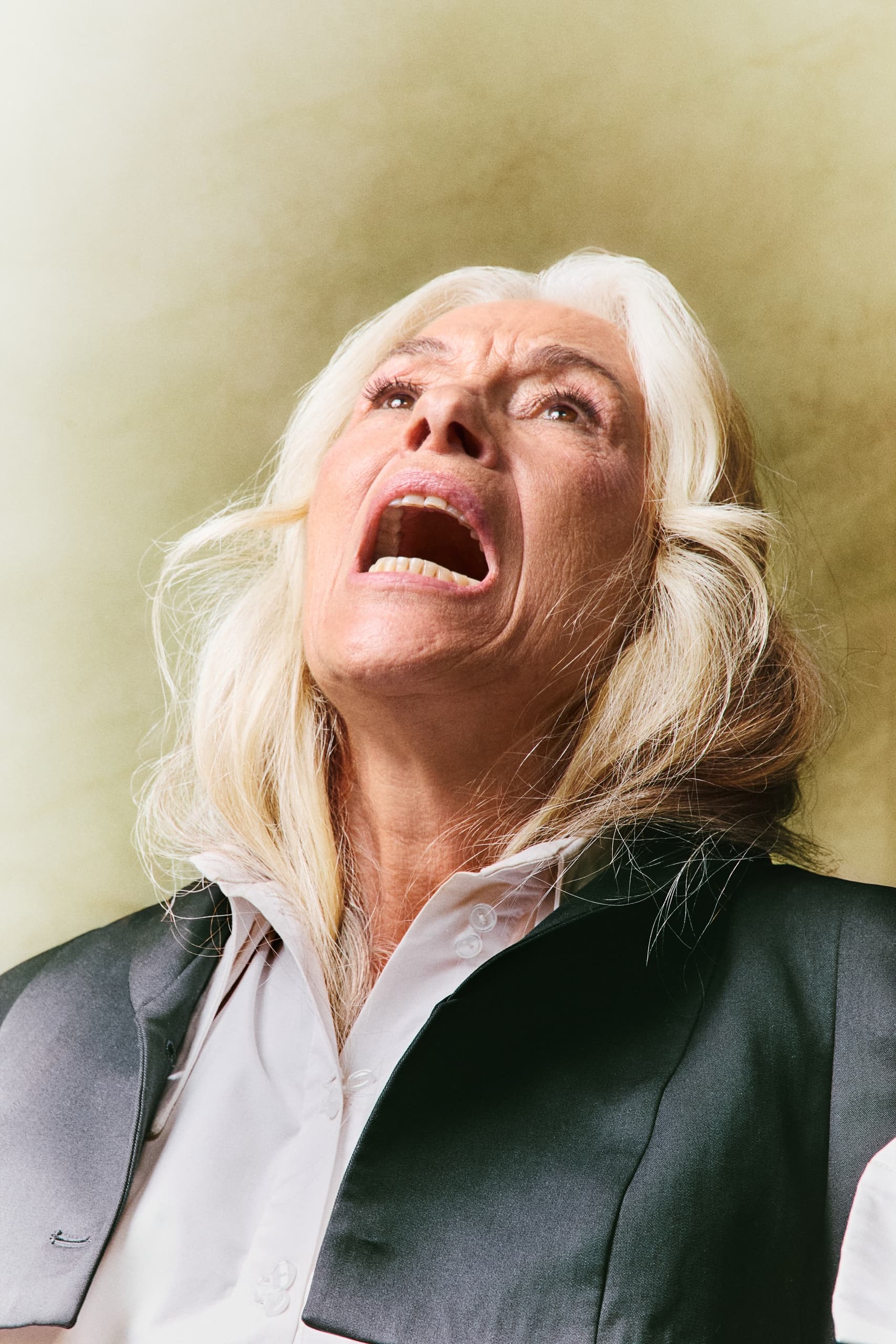 Elderly woman expressing emotion with mouth open, wearing formal attire.