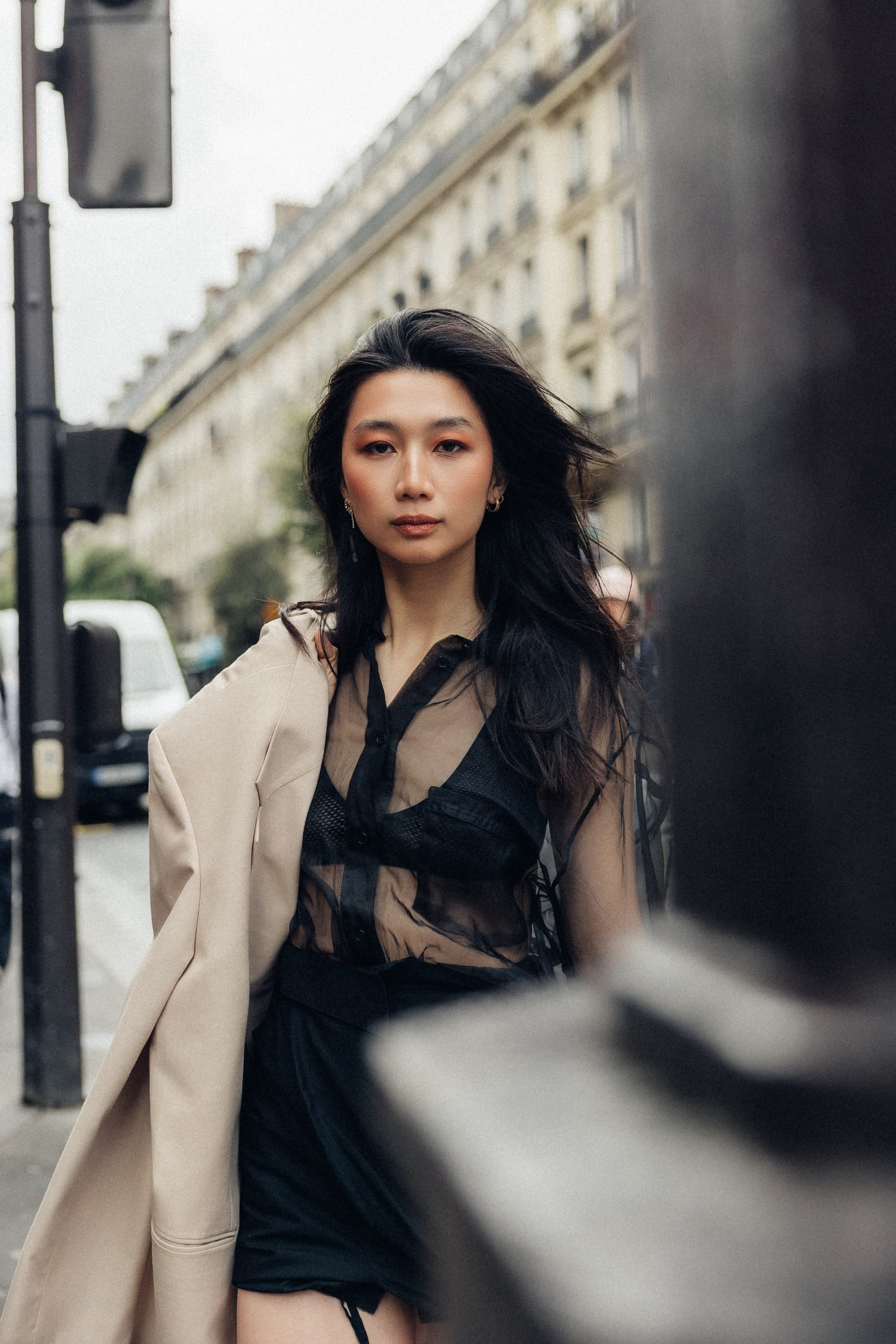Stylish woman in sheer outfit walking down a Parisian street.