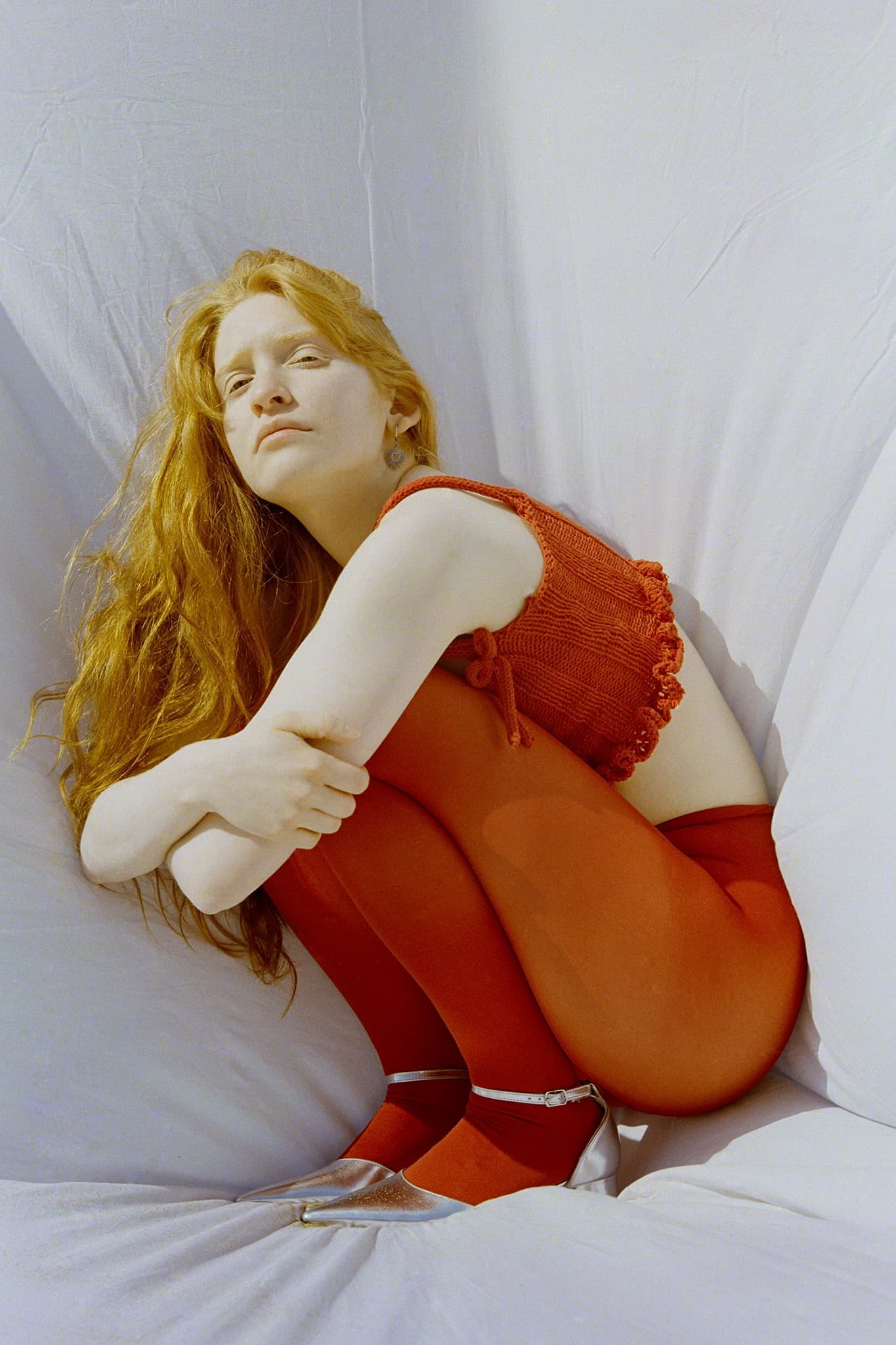 Young woman in red tights and top sitting against a white backdrop.