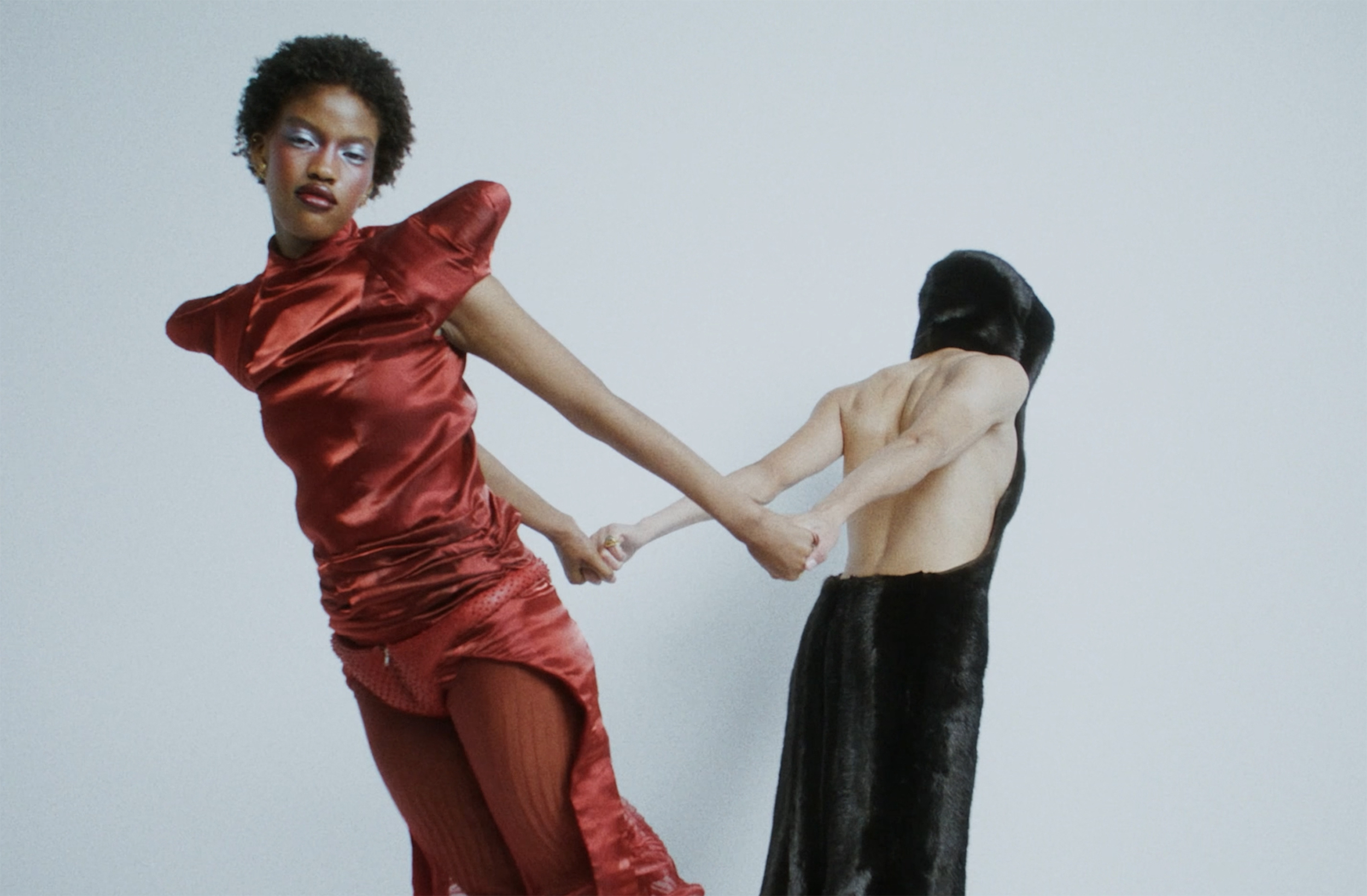 Two models holding hands in striking red and black outfits.