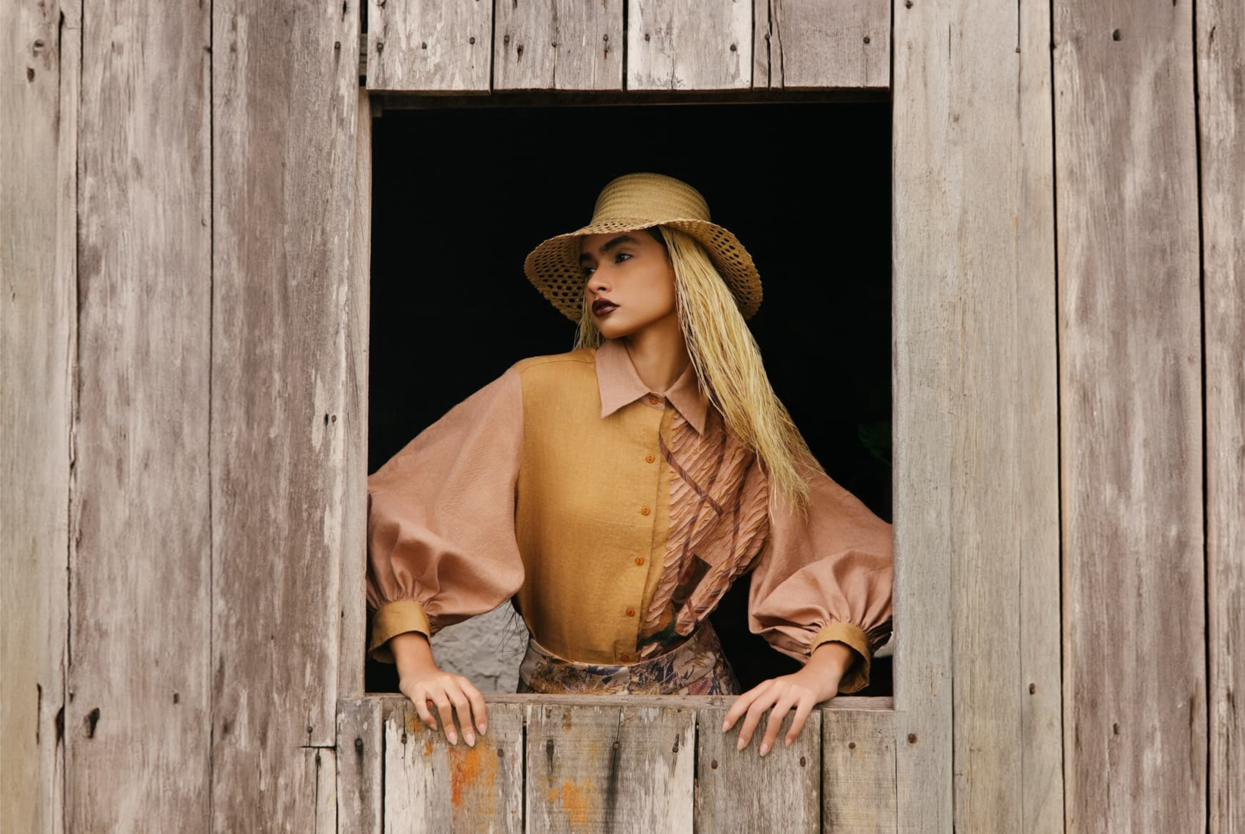 Fashionable woman in rustic window frame, wearing vintage outfit and straw hat.