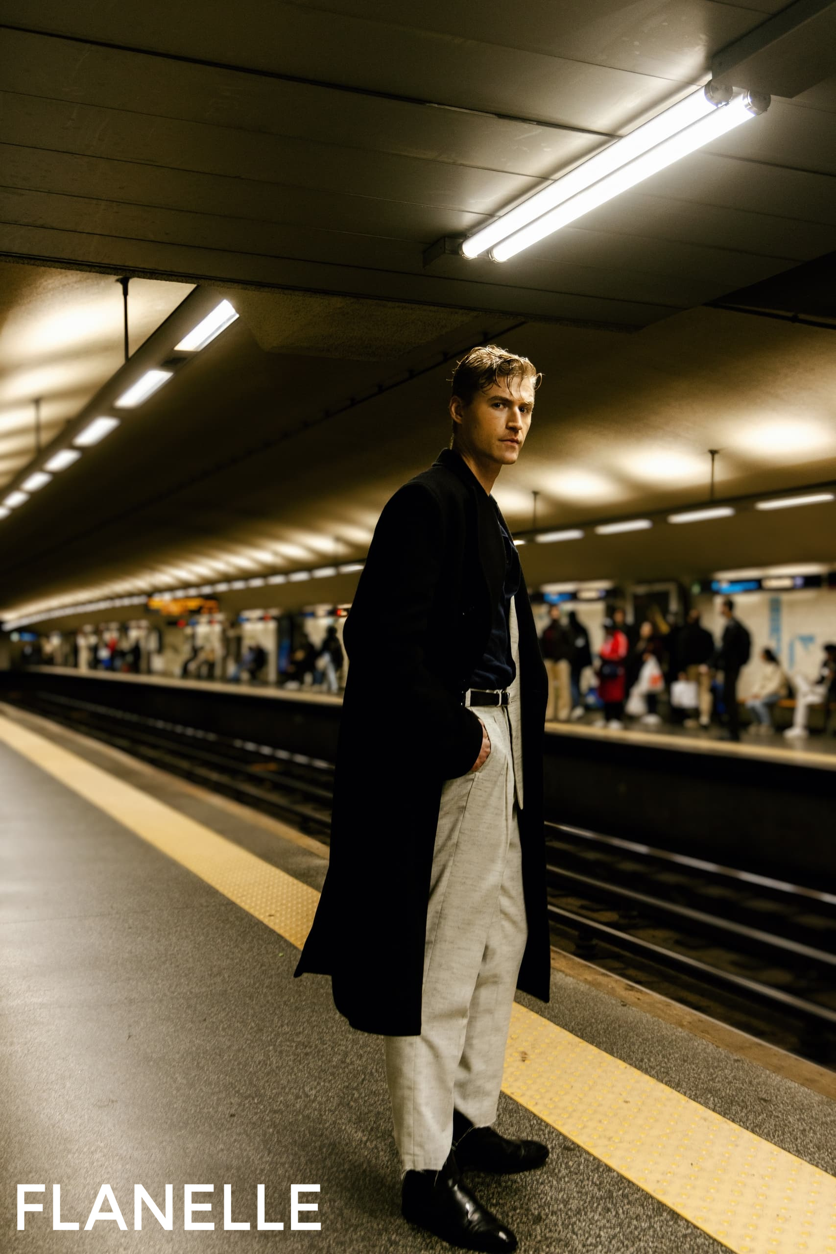 Man in stylish outfit waiting at subway station platform.