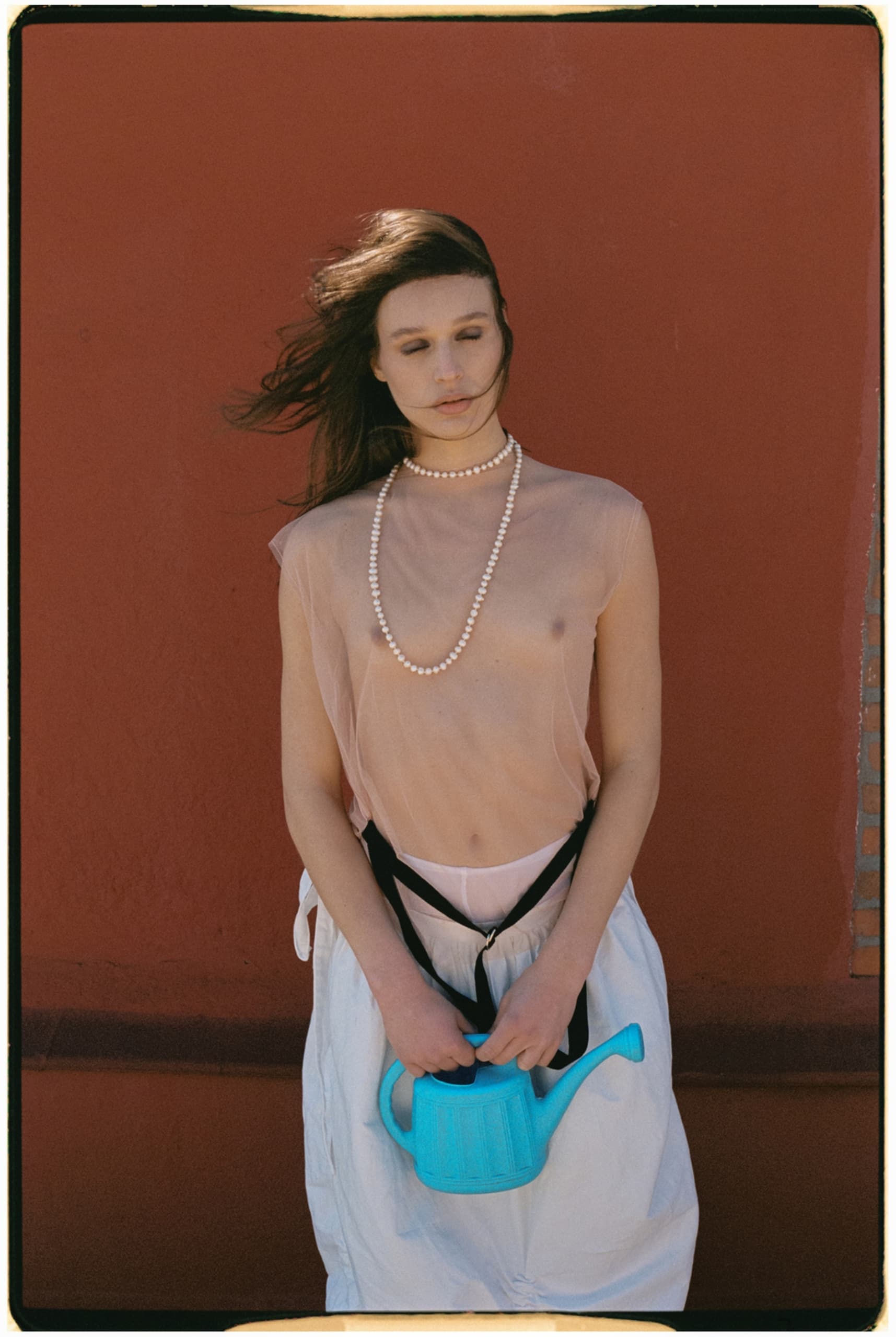 Woman holding a blue watering can in front of a red wall.