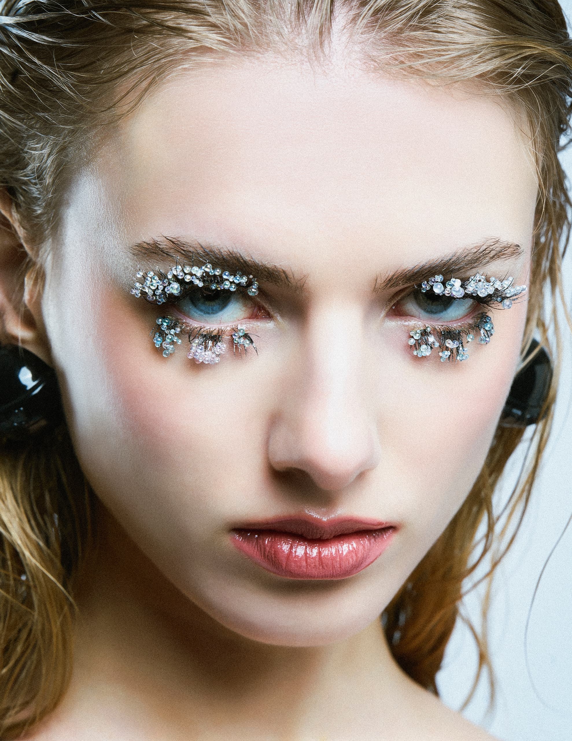 Close-up of a woman with creative crystal eye makeup and glossy lips.