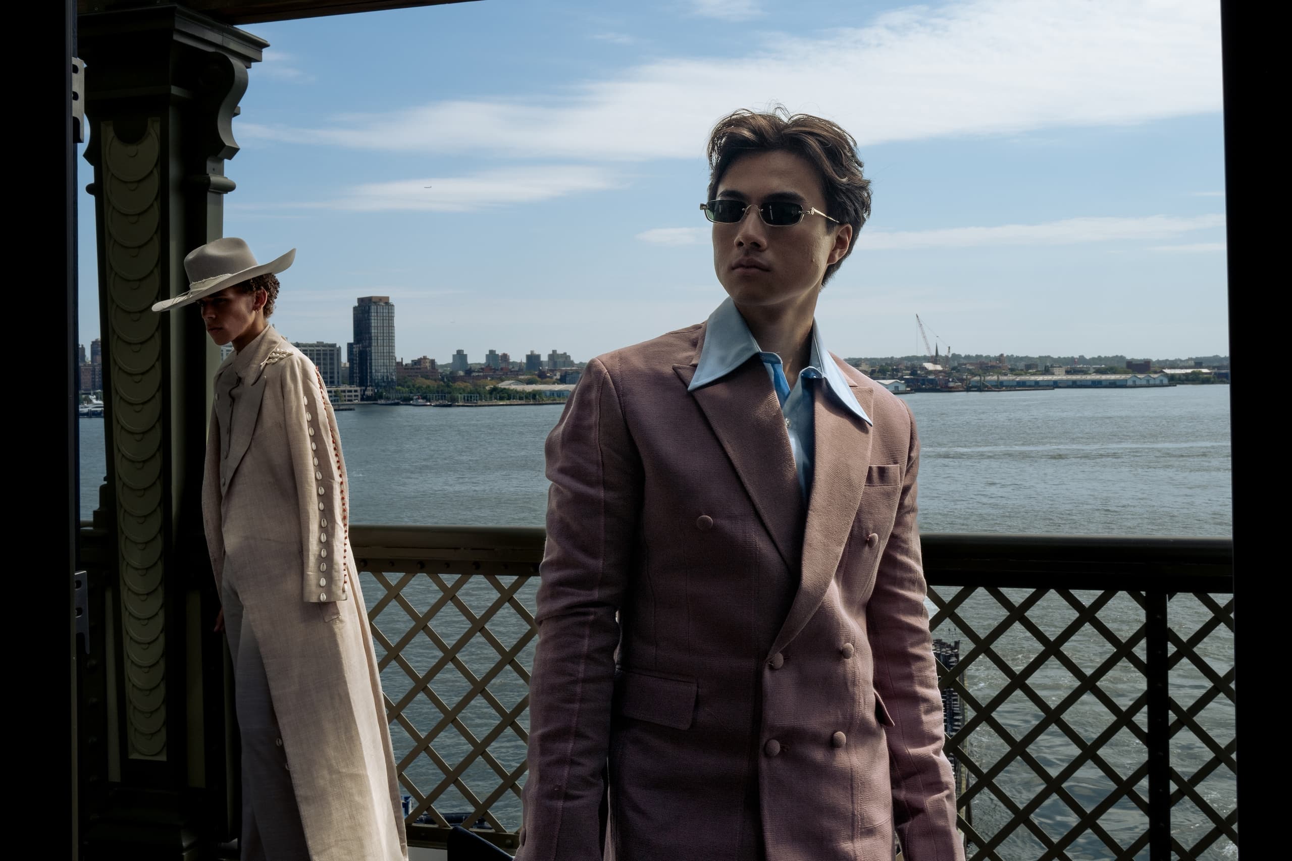 Stylish models in suits by the waterfront under a blue sky.