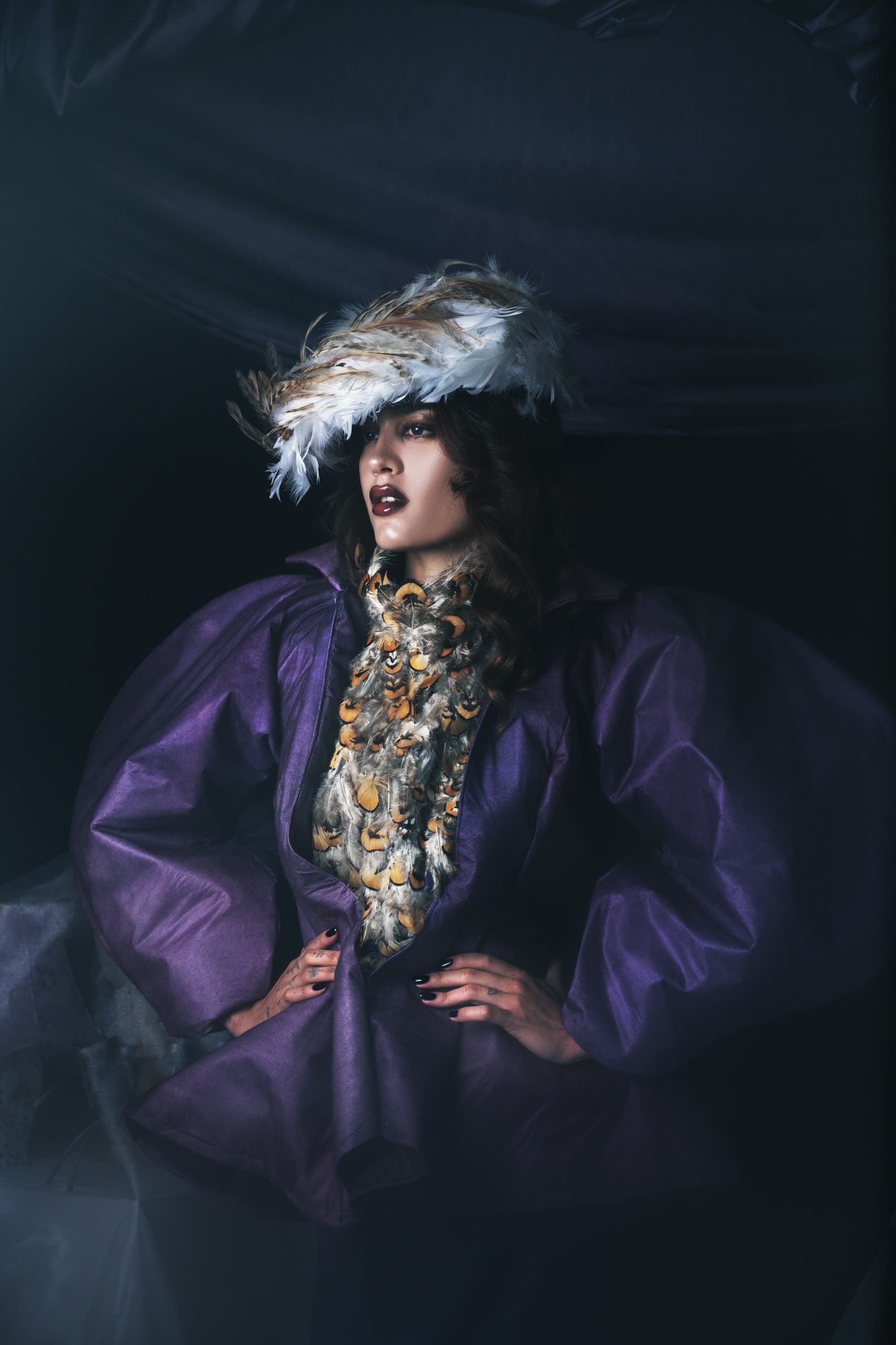Fashionable woman in elaborate feather hat and purple outfit.