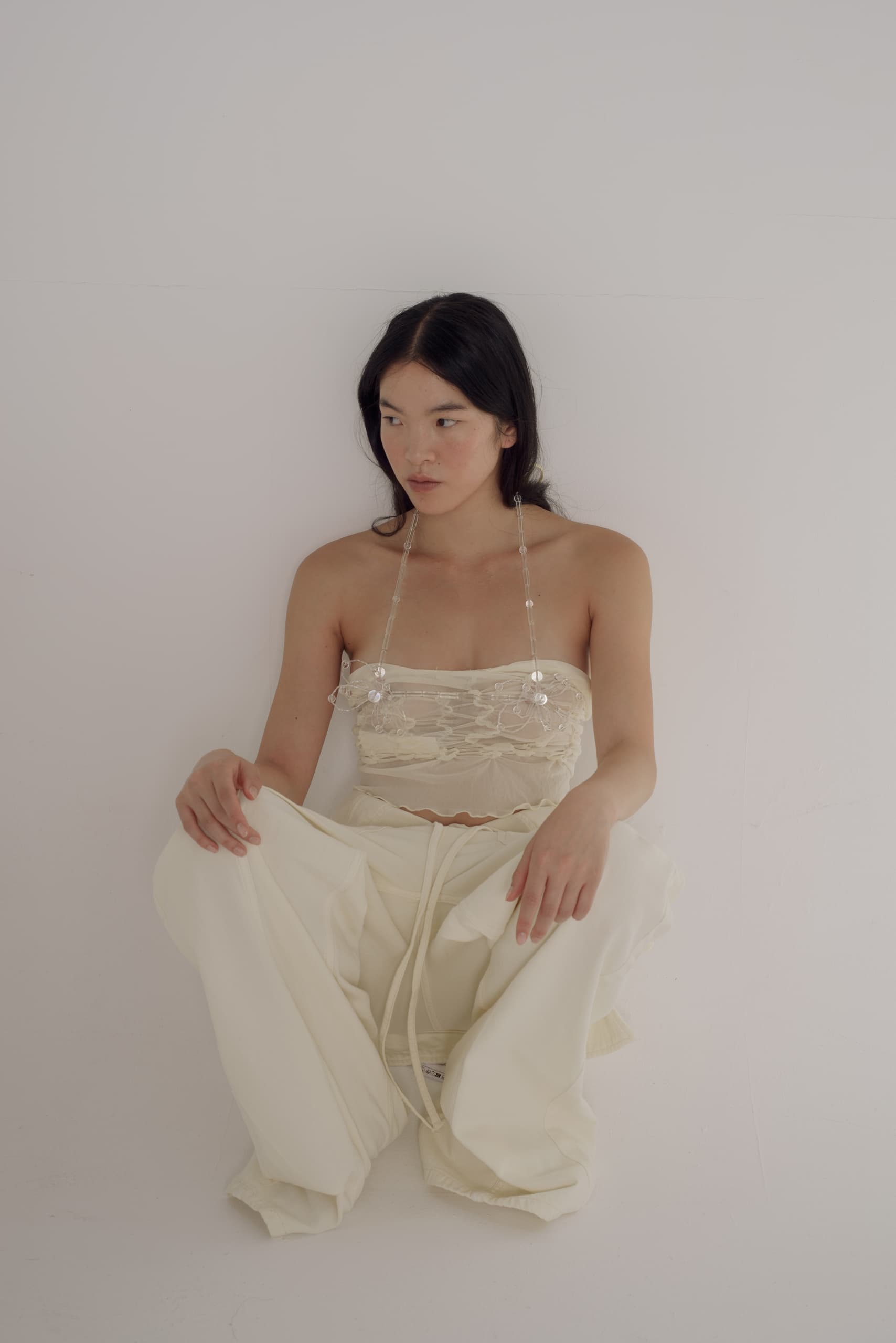 Woman in white fashion ensemble sitting against a minimalistic white background.