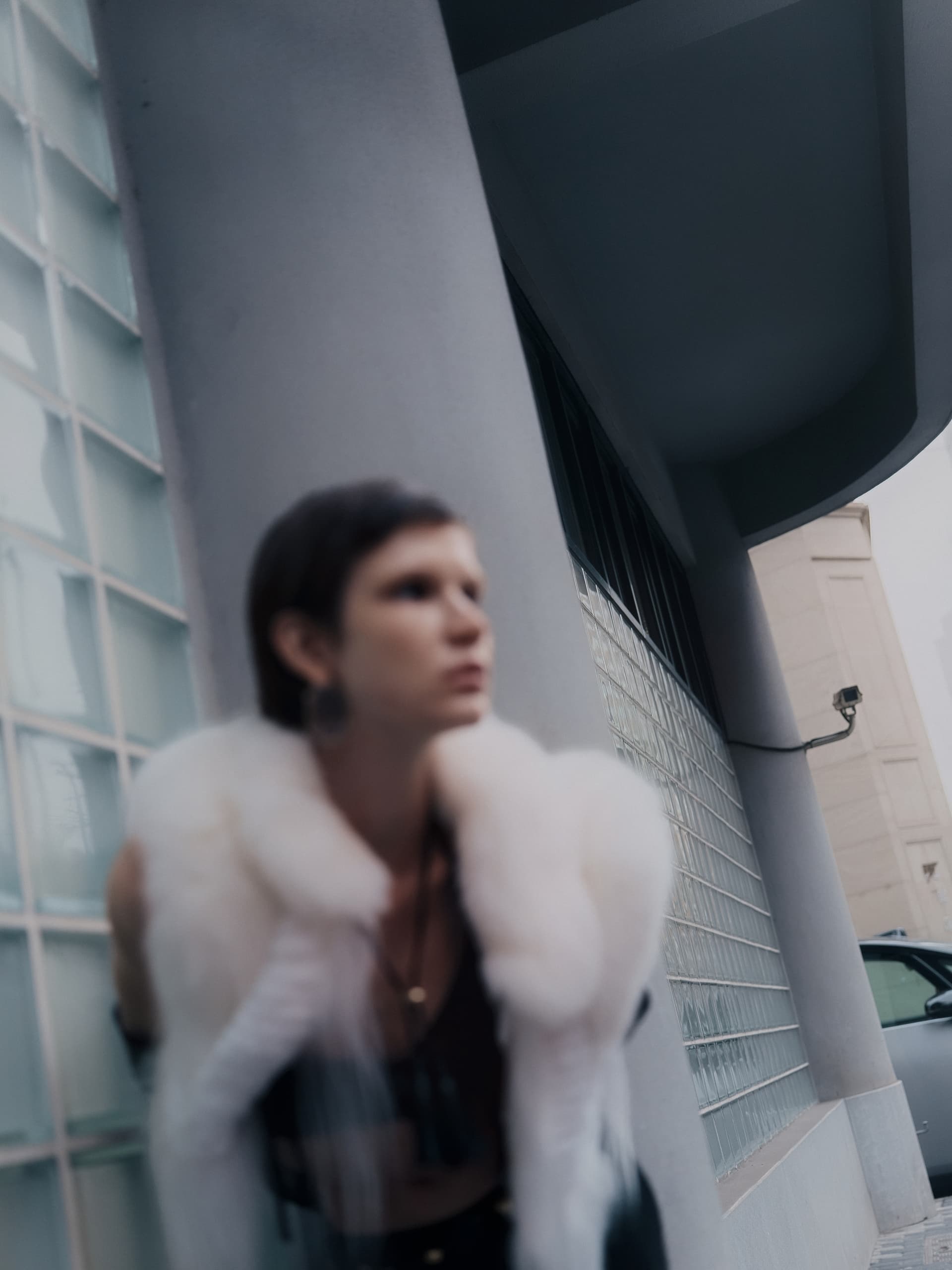Blurry figure in fur coat near modern glass building wall.