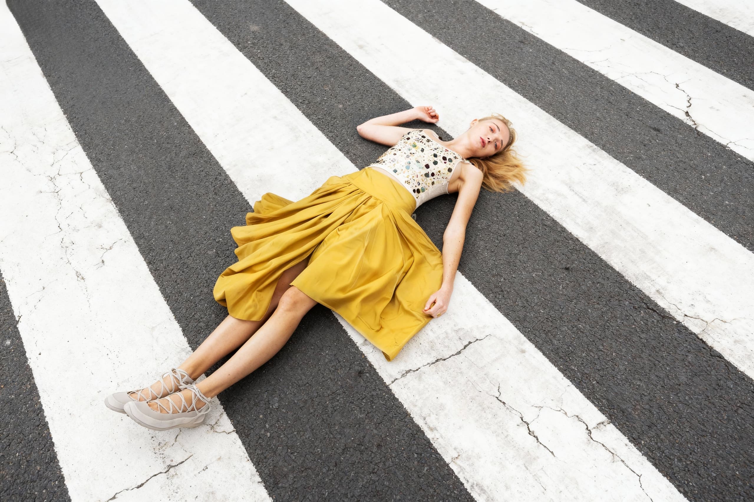Woman in yellow skirt lying on a crosswalk, artistic street photography.