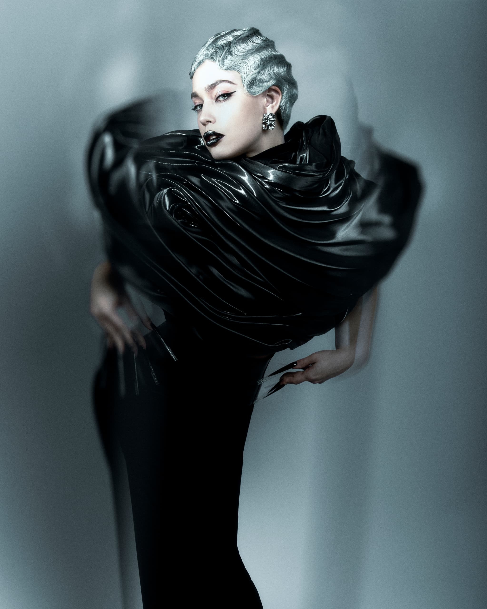 Avant-garde fashion model in dramatic black attire with sleek, silver hair.