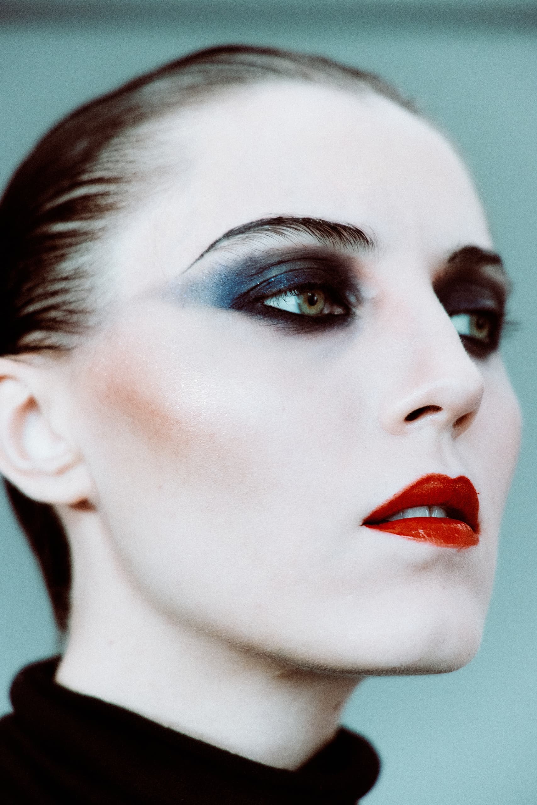 Close-up of a model with bold makeup, featuring red lips and smokey eyeshadow.