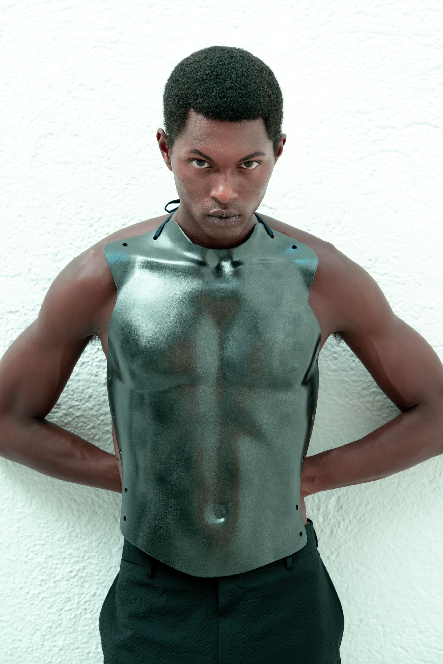 Model posing in metallic chest armor against a white textured background.