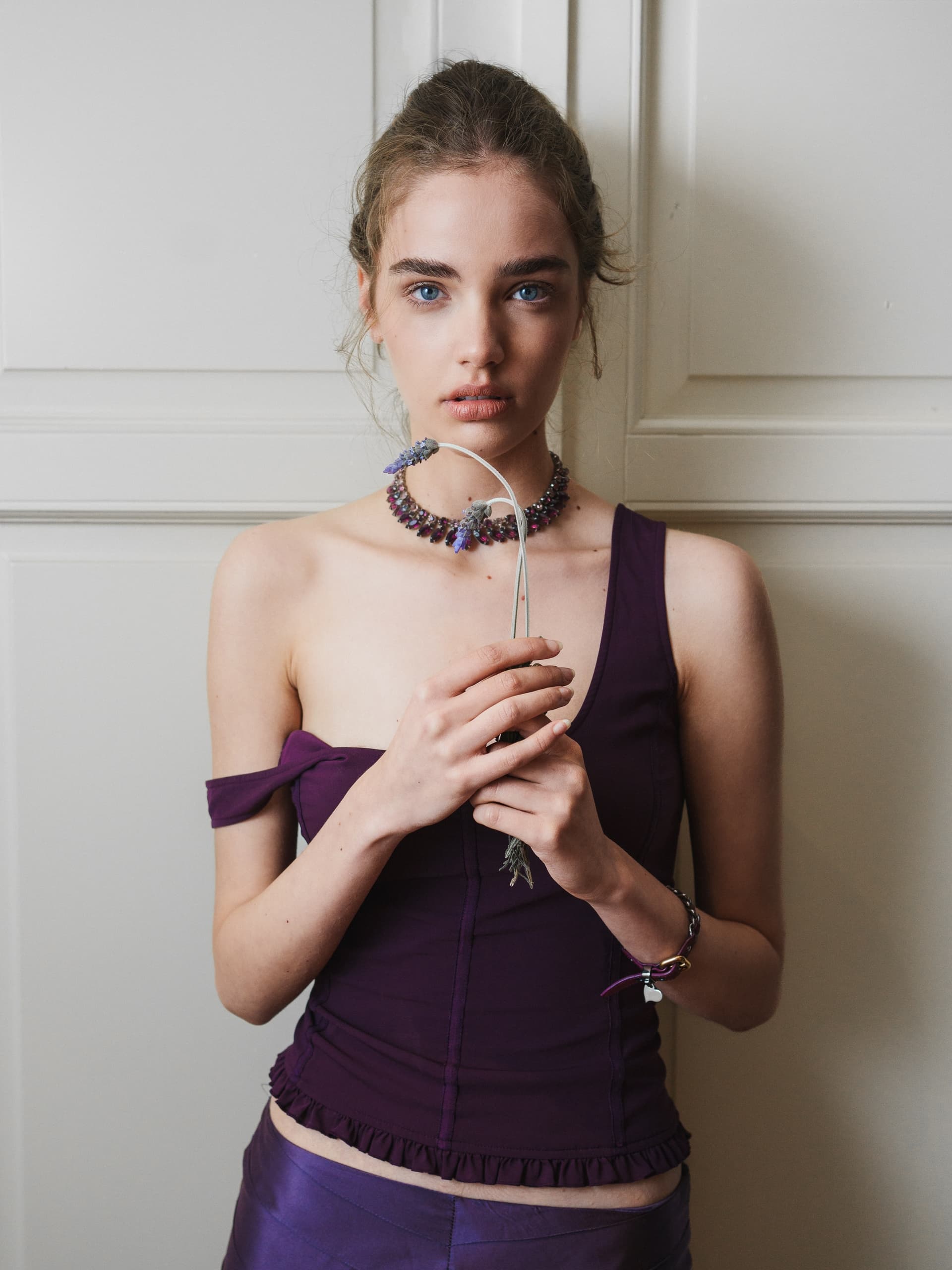 Woman in purple outfit holding lavender in front of white door.
