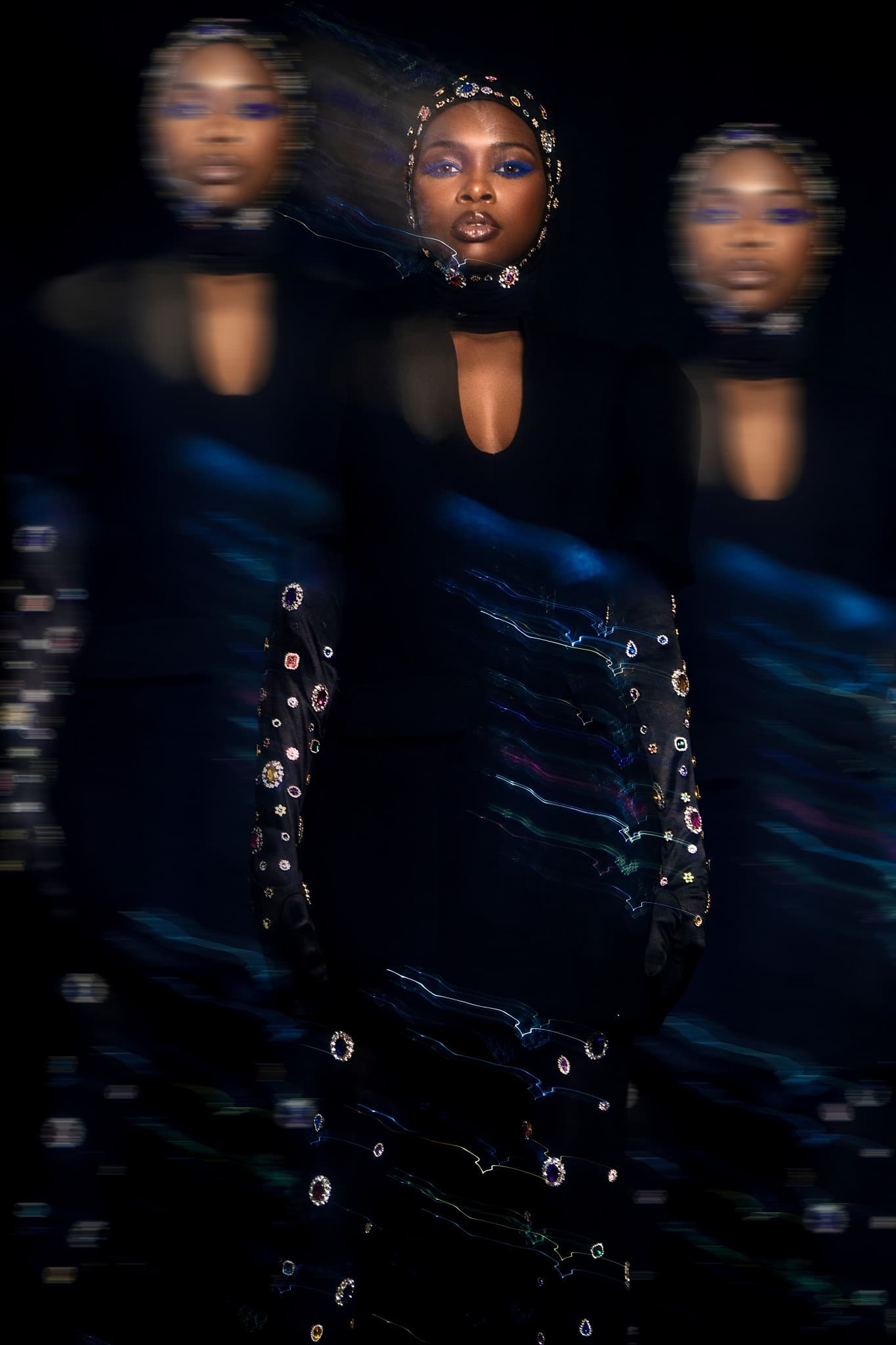 Artistic portrait with motion blur and jewel-adorned clothing on a dark background.