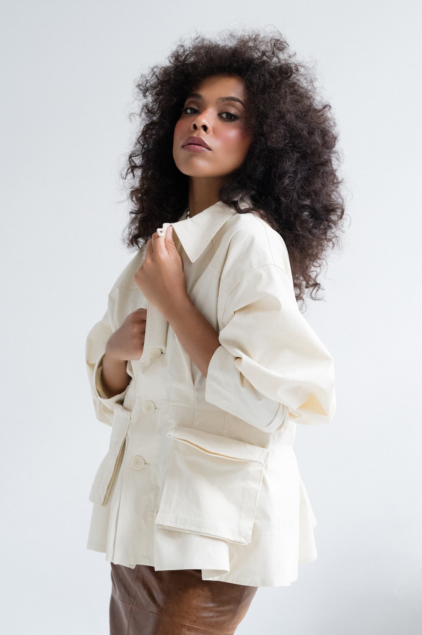 Woman in stylish beige jacket with curly hair poses confidently.