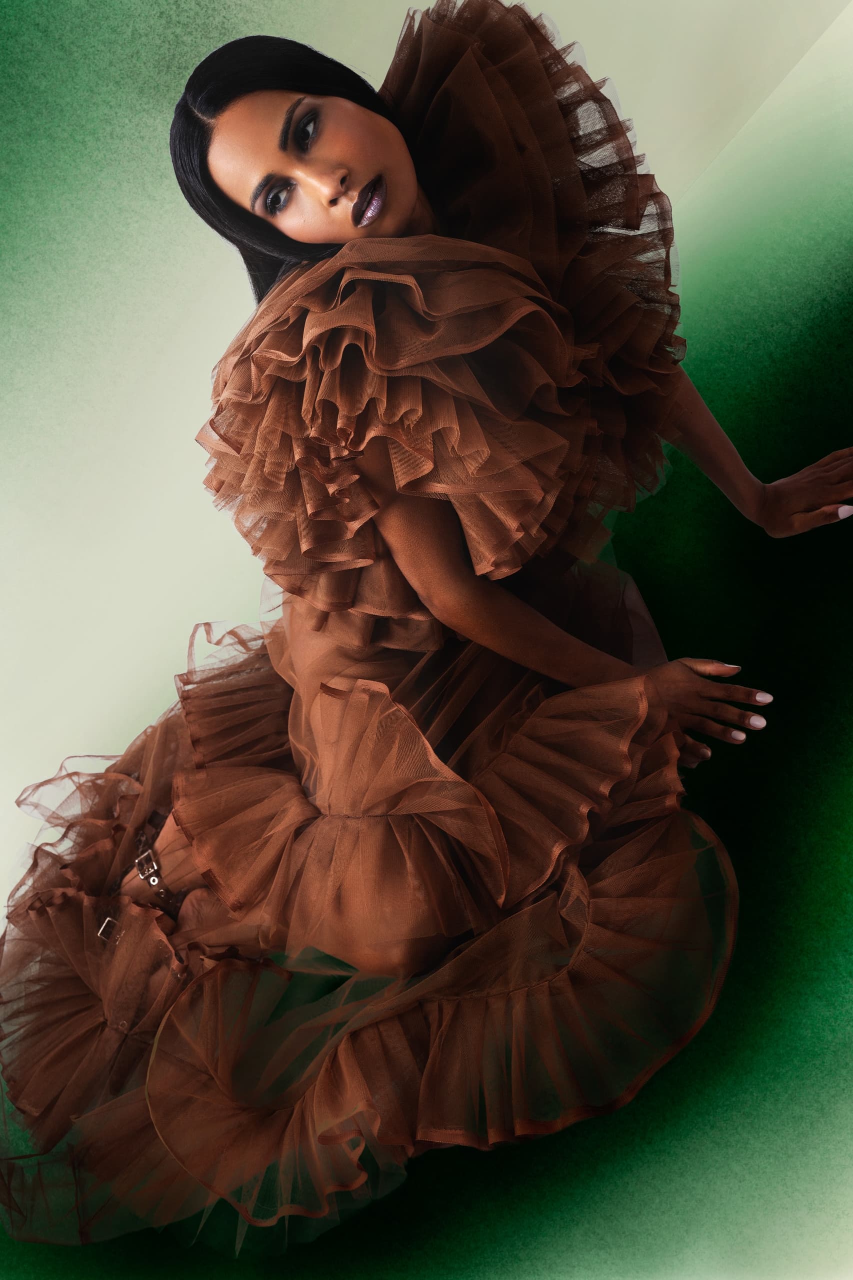 Elegant woman in a layered brown tulle gown on a green gradient background.