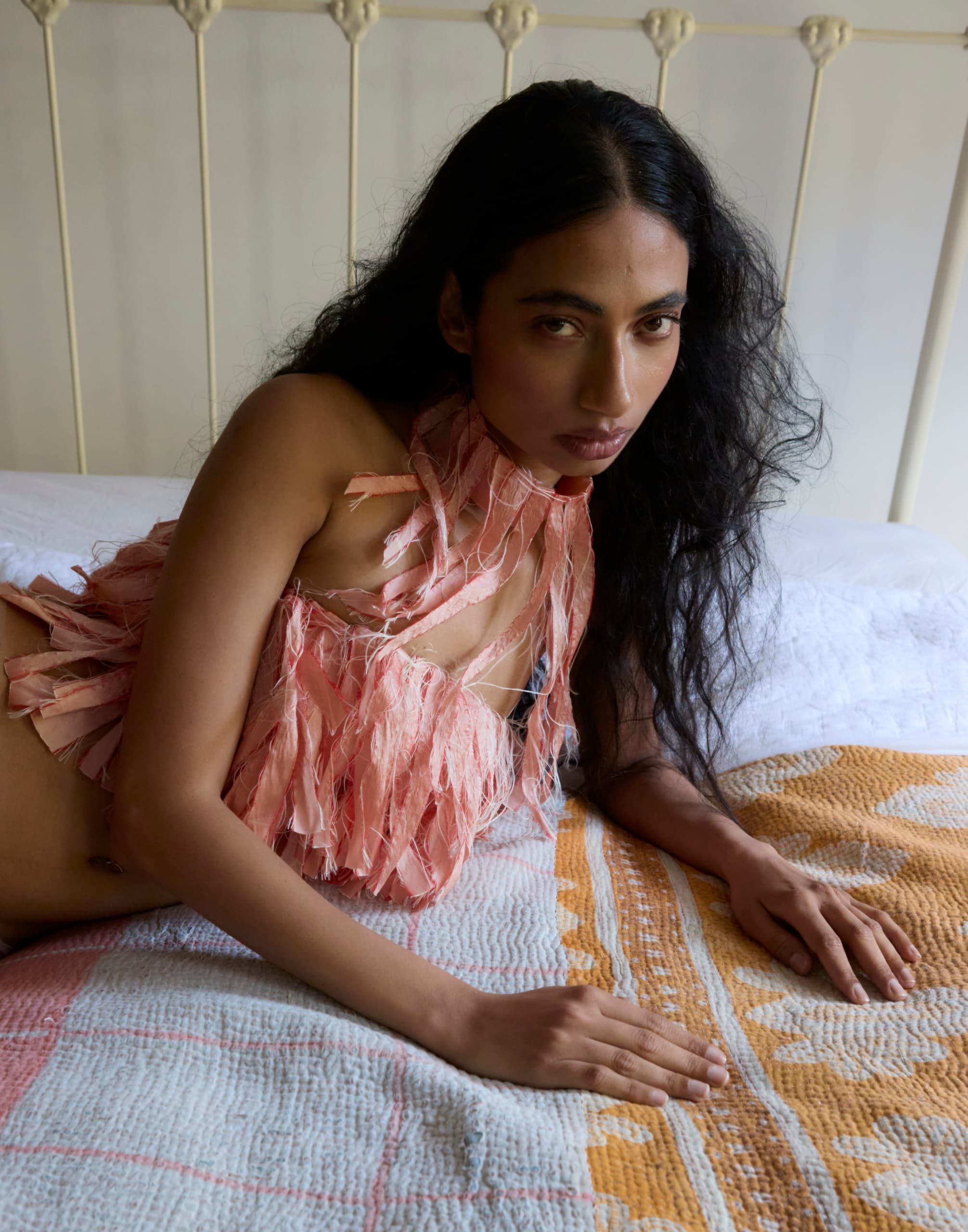 Woman in a pink fringe top lying on a patterned bedspread.