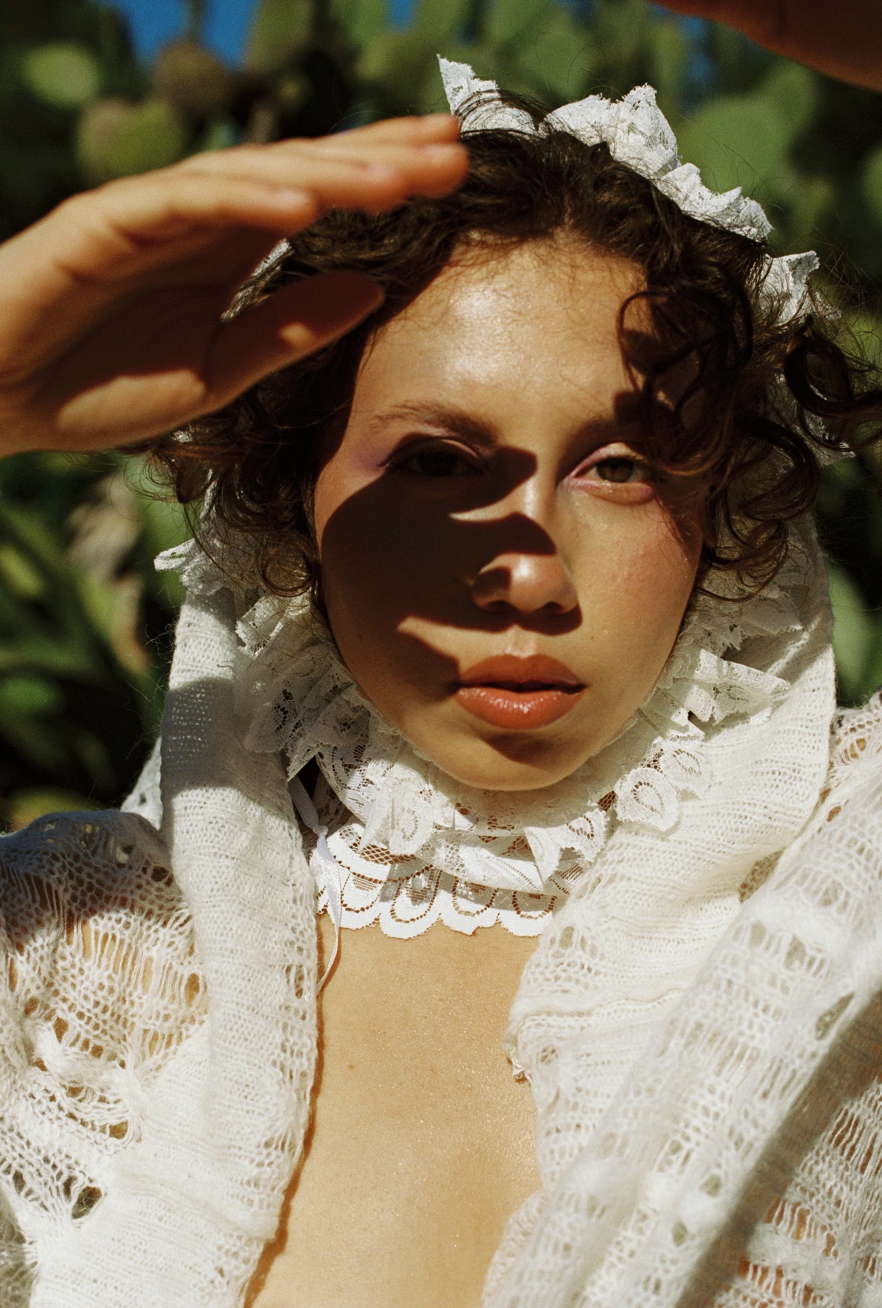Woman in lace garment shielding eyes from sun with hand.