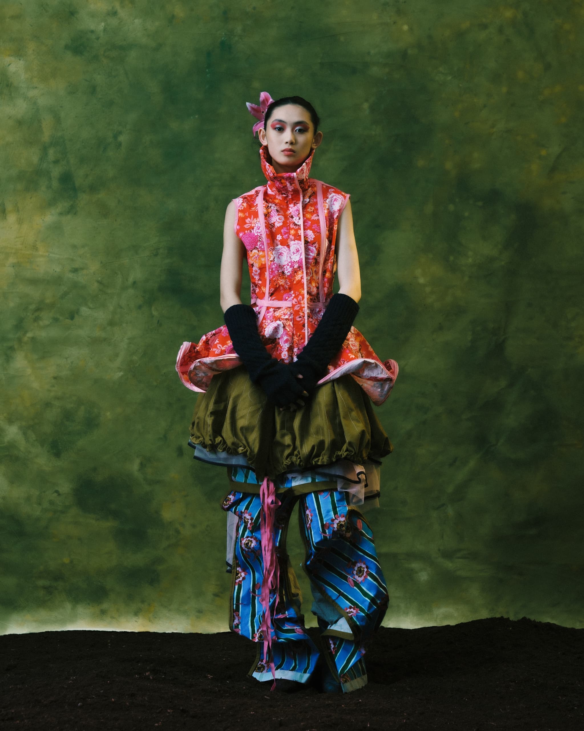 Fashion model in vibrant floral and striped gown against a green backdrop.