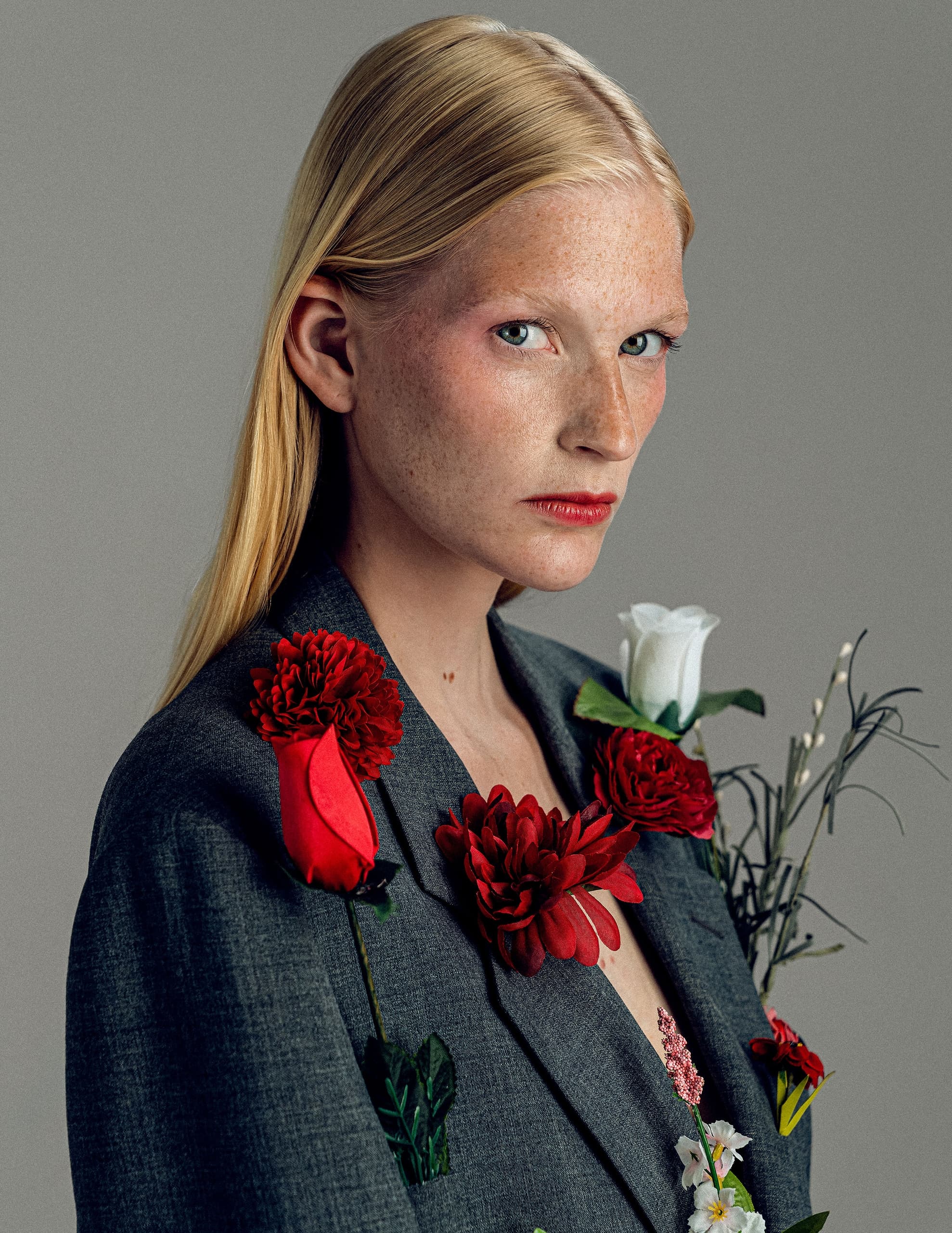 Person with flowers on gray blazer, serious expression, artistic portrait.
