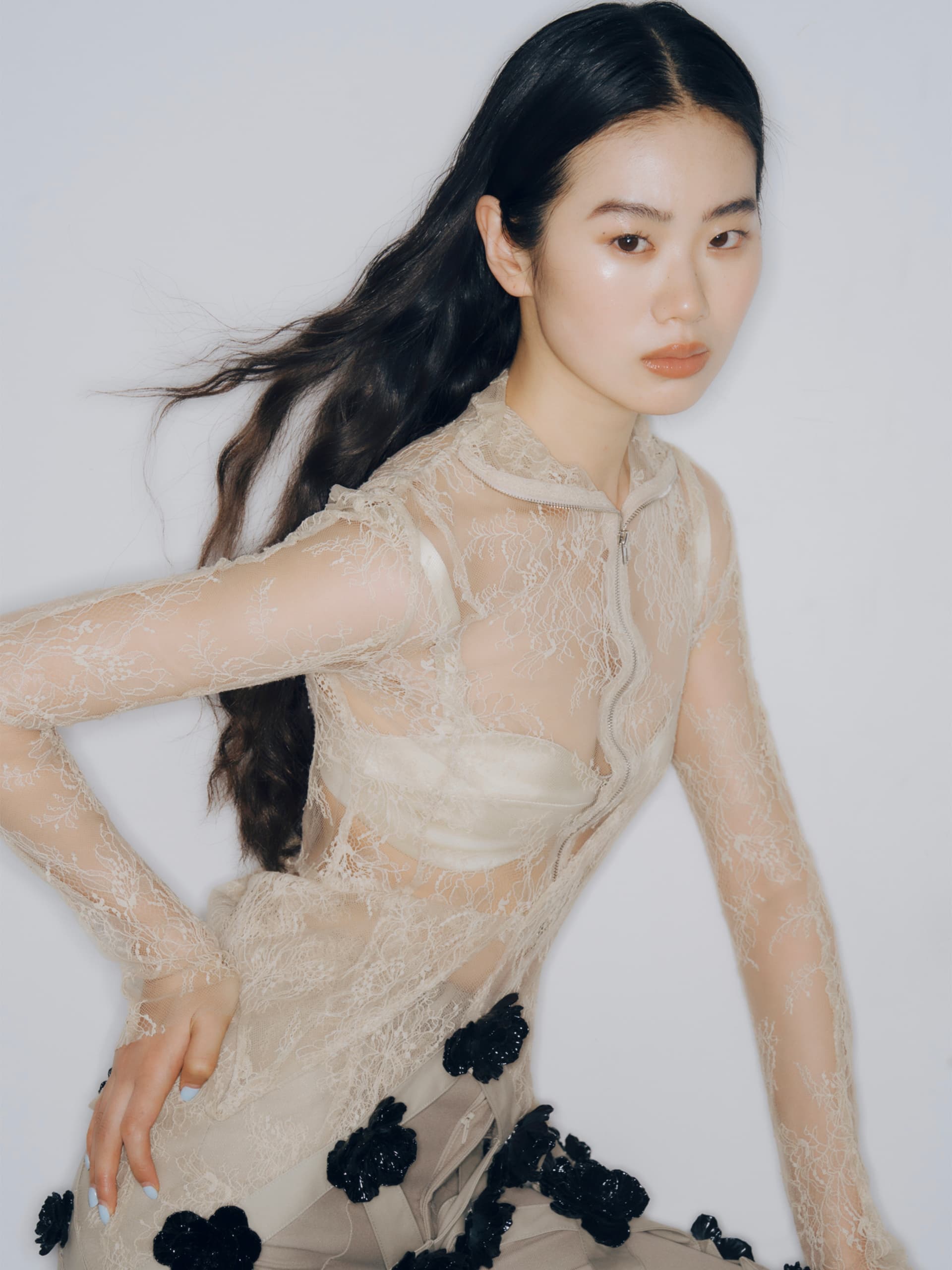 Woman in a sheer lace top with floral accents, styled for a fashion photoshoot.