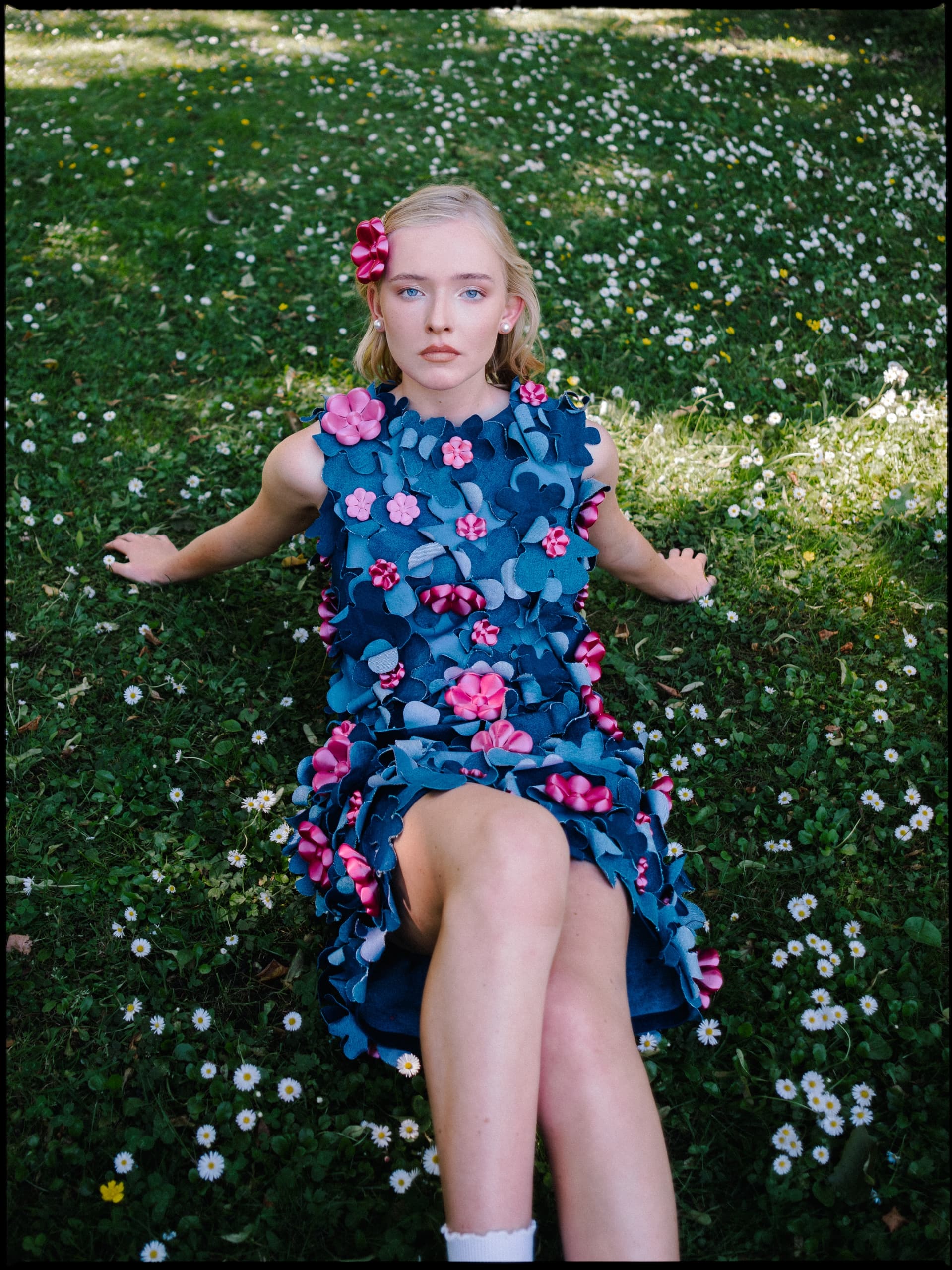 Woman in floral dress lounging on grass, surrounded by daisies.