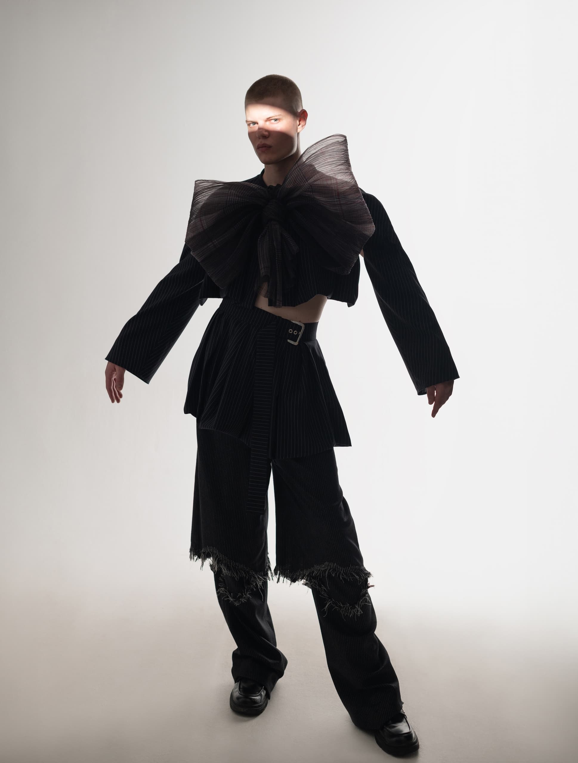 Model in avant-garde black outfit with large bow, striking fashion pose.