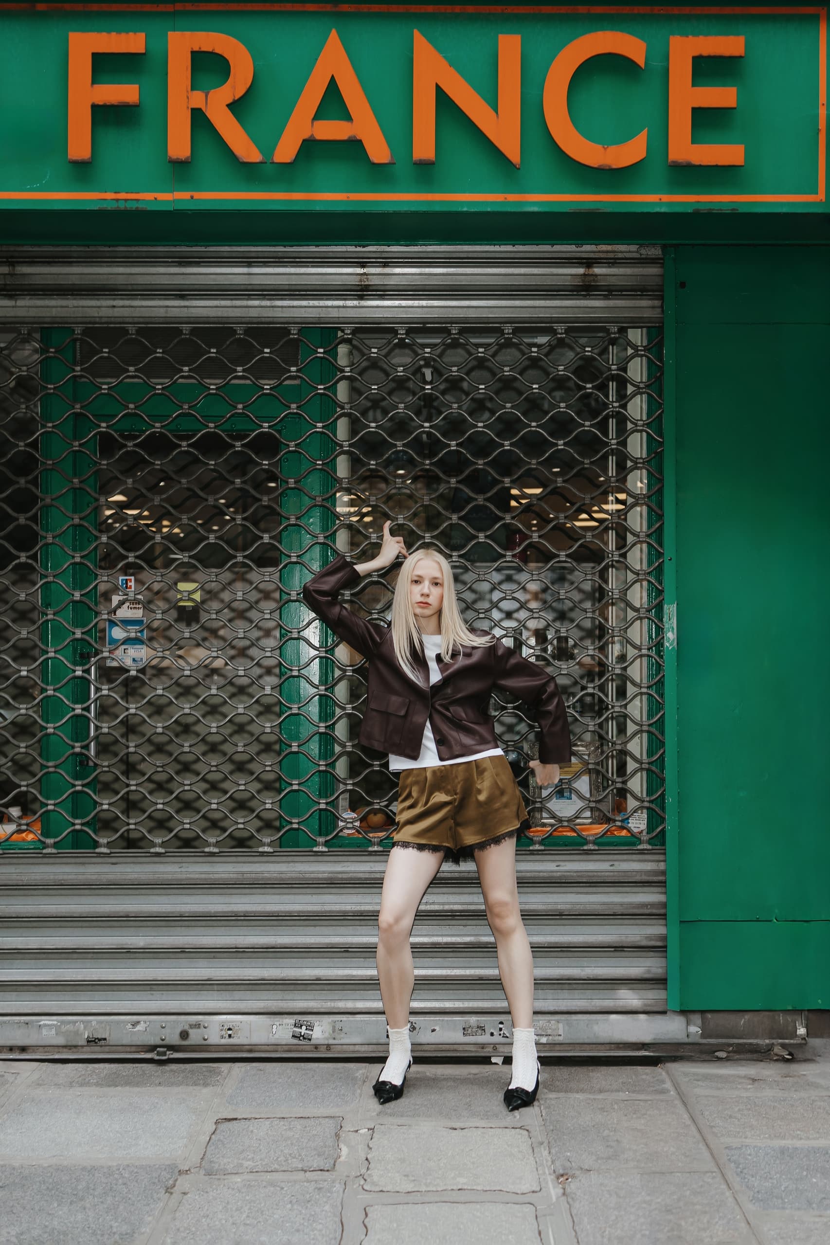Fashionable woman poses in front of a closed French storefront with green decor.