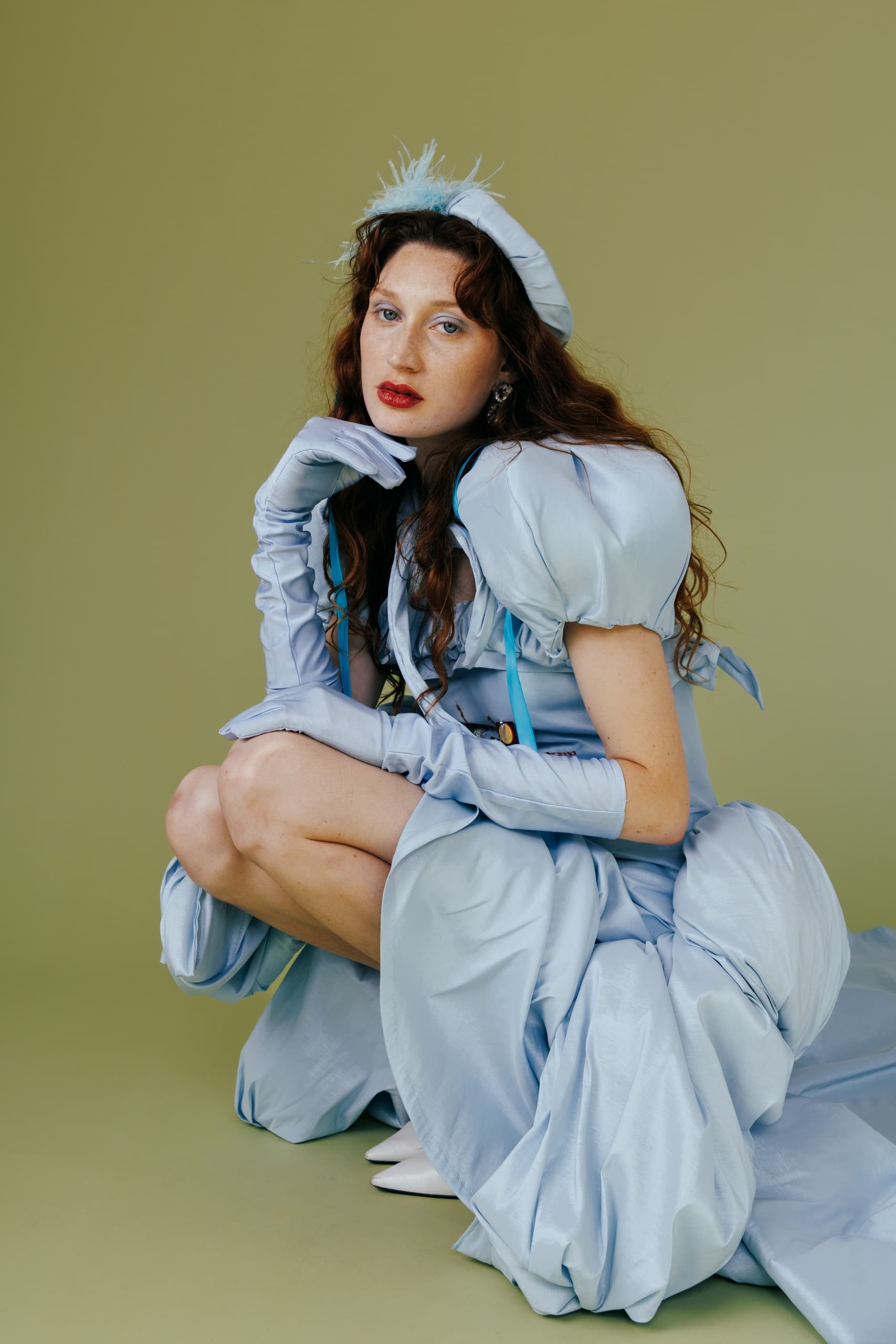 Person in elegant blue dress with gloves, posing on green background.