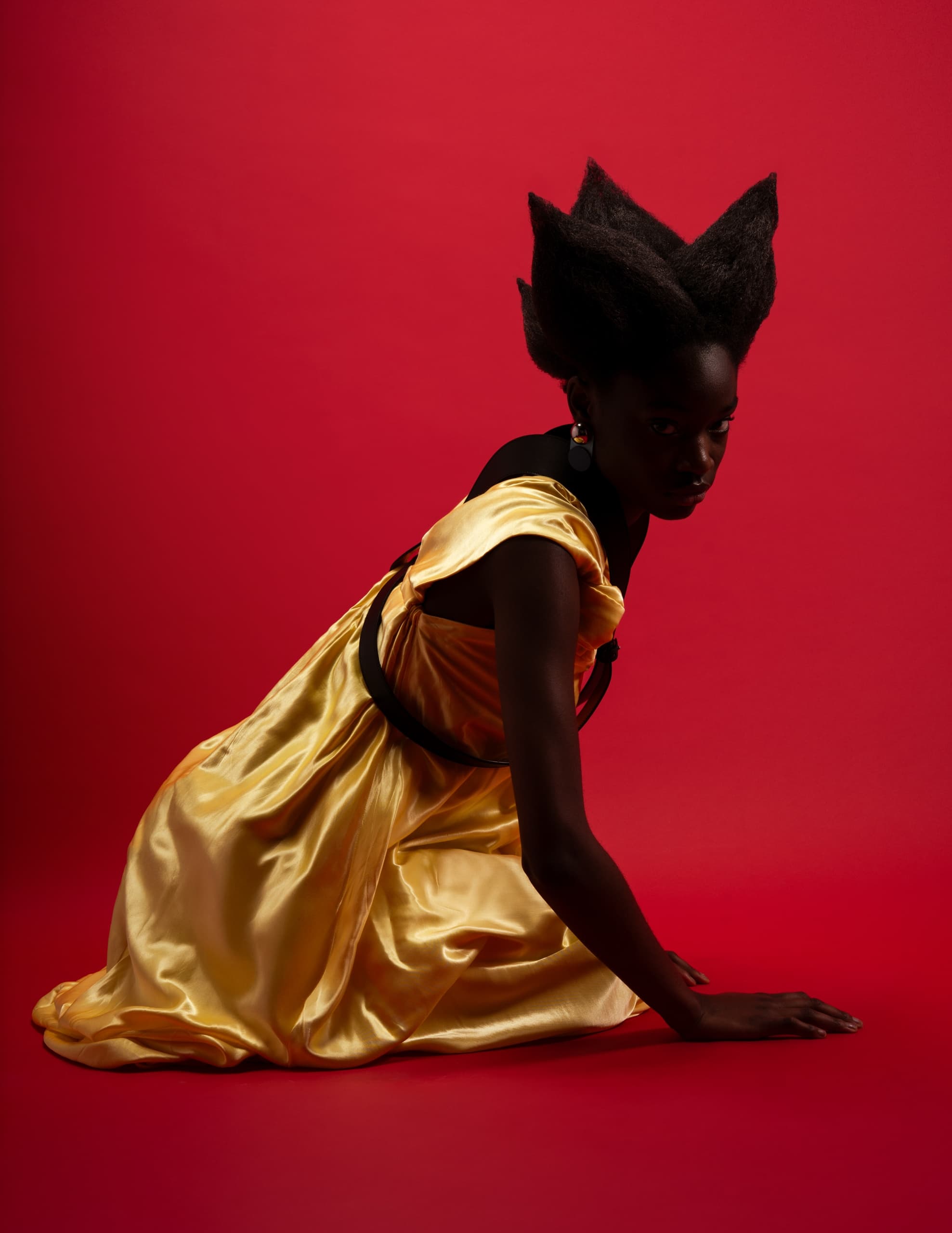 Model in gold dress with unique hairstyle against a bold red background.