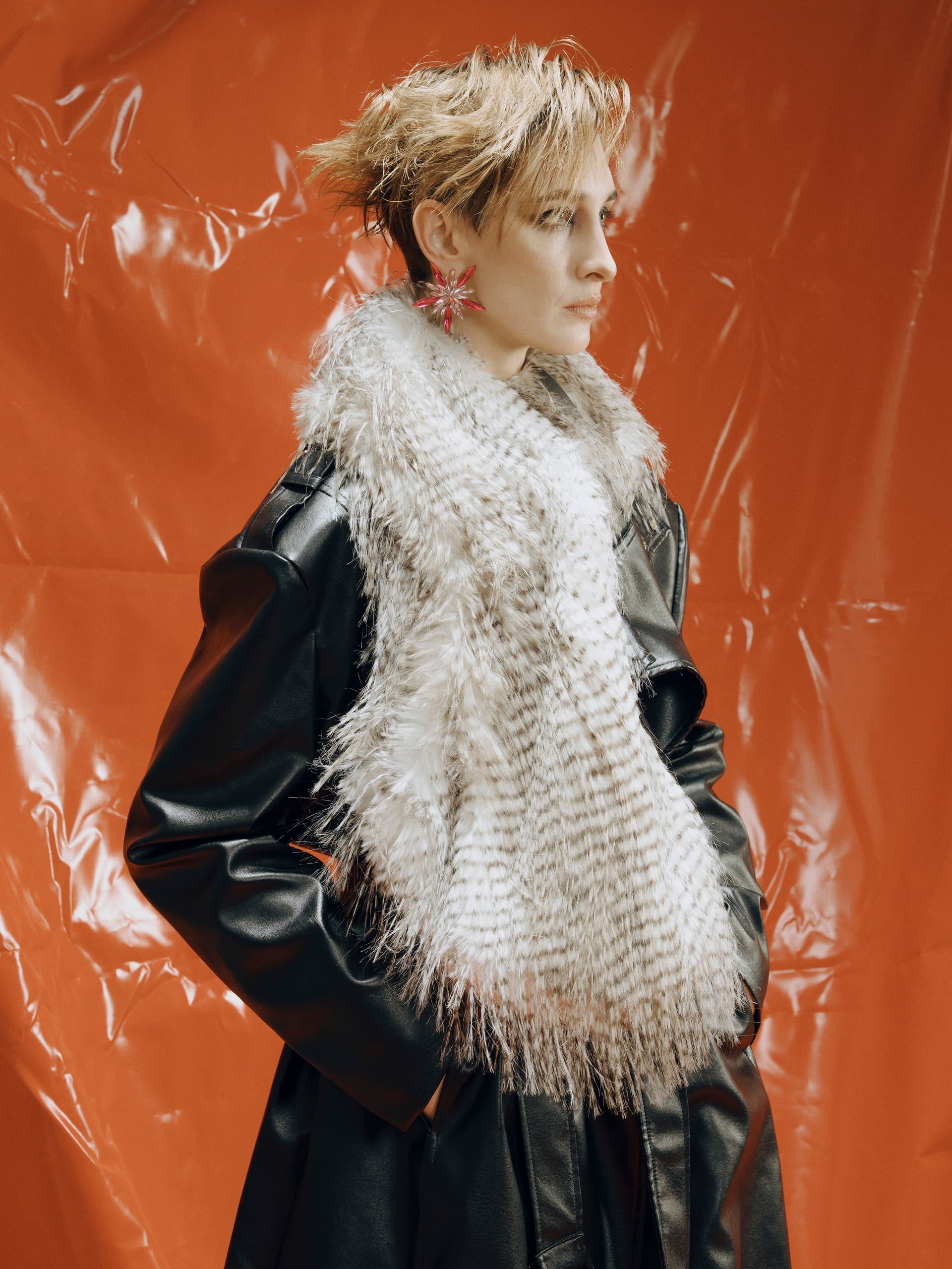 Fashionable model in fur scarf and leather coat against an orange backdrop.
