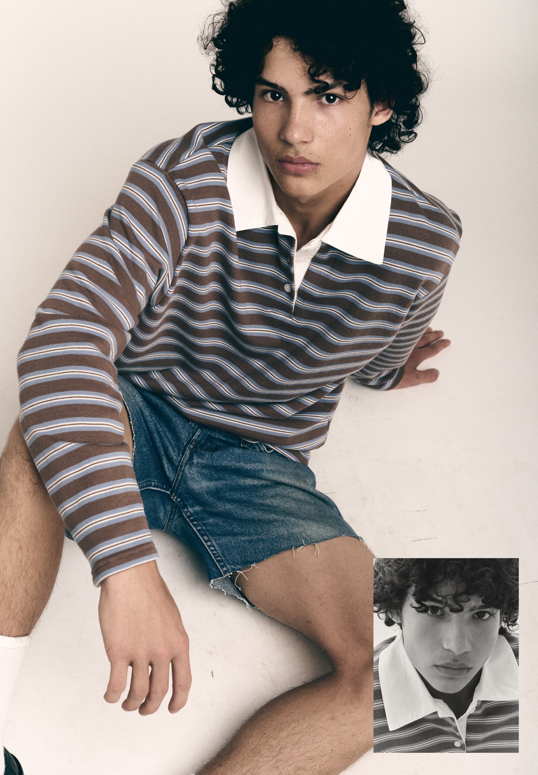 Young man in striped rugby shirt and denim shorts sitting casually.