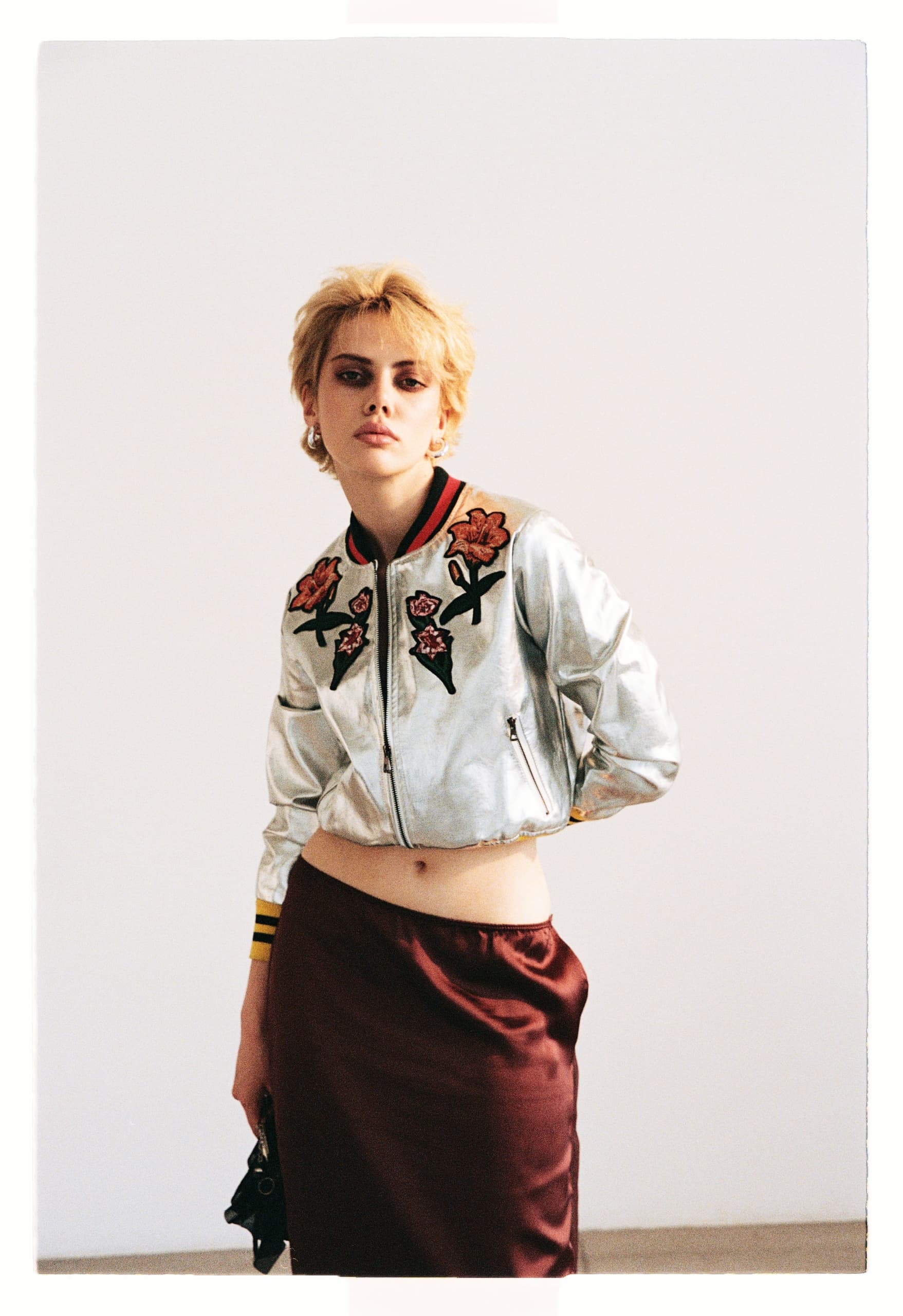 Woman in floral bomber jacket and burgundy skirt posing confidently.