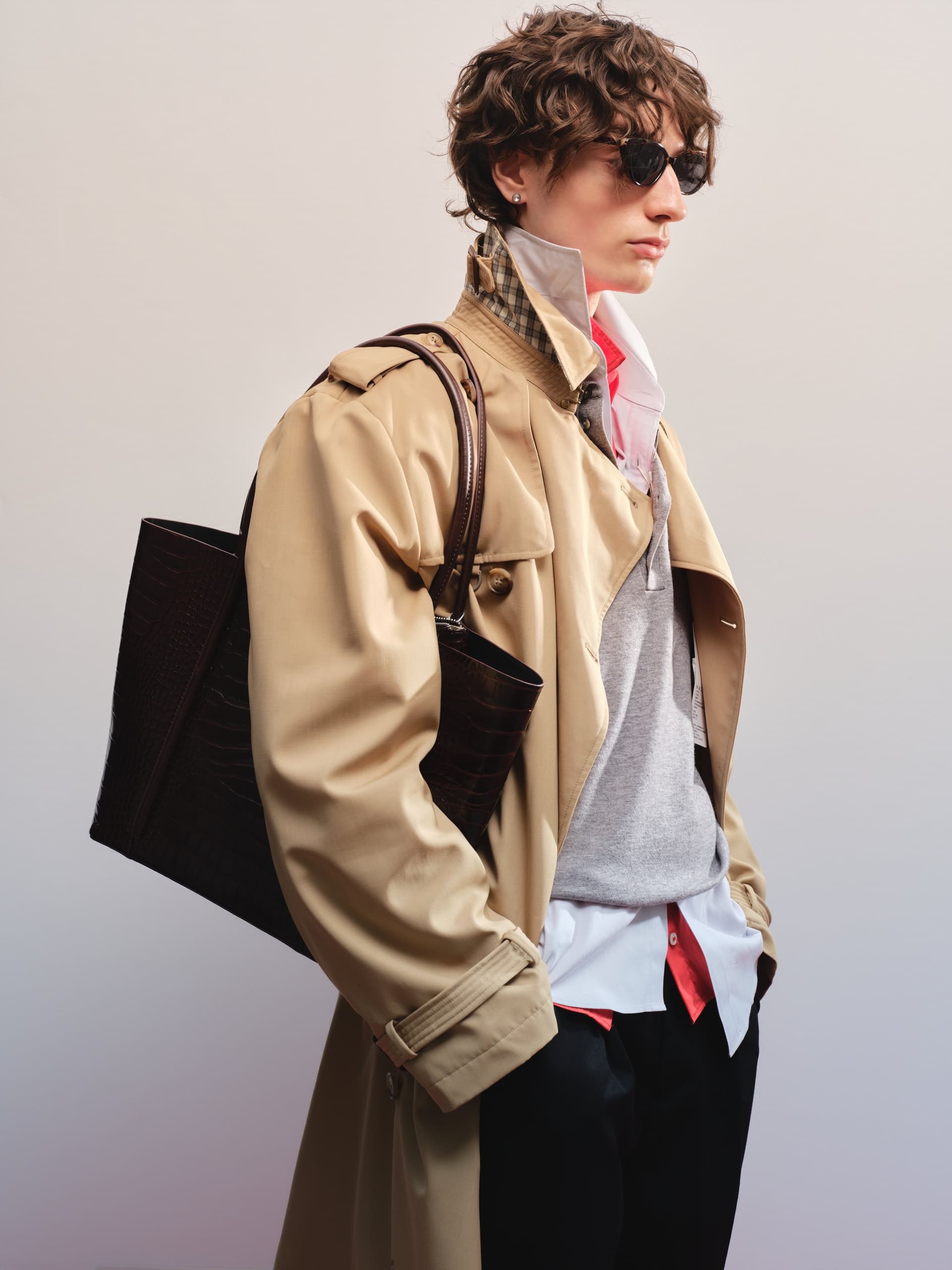 Stylish person in a trench coat with sunglasses and a leather bag.