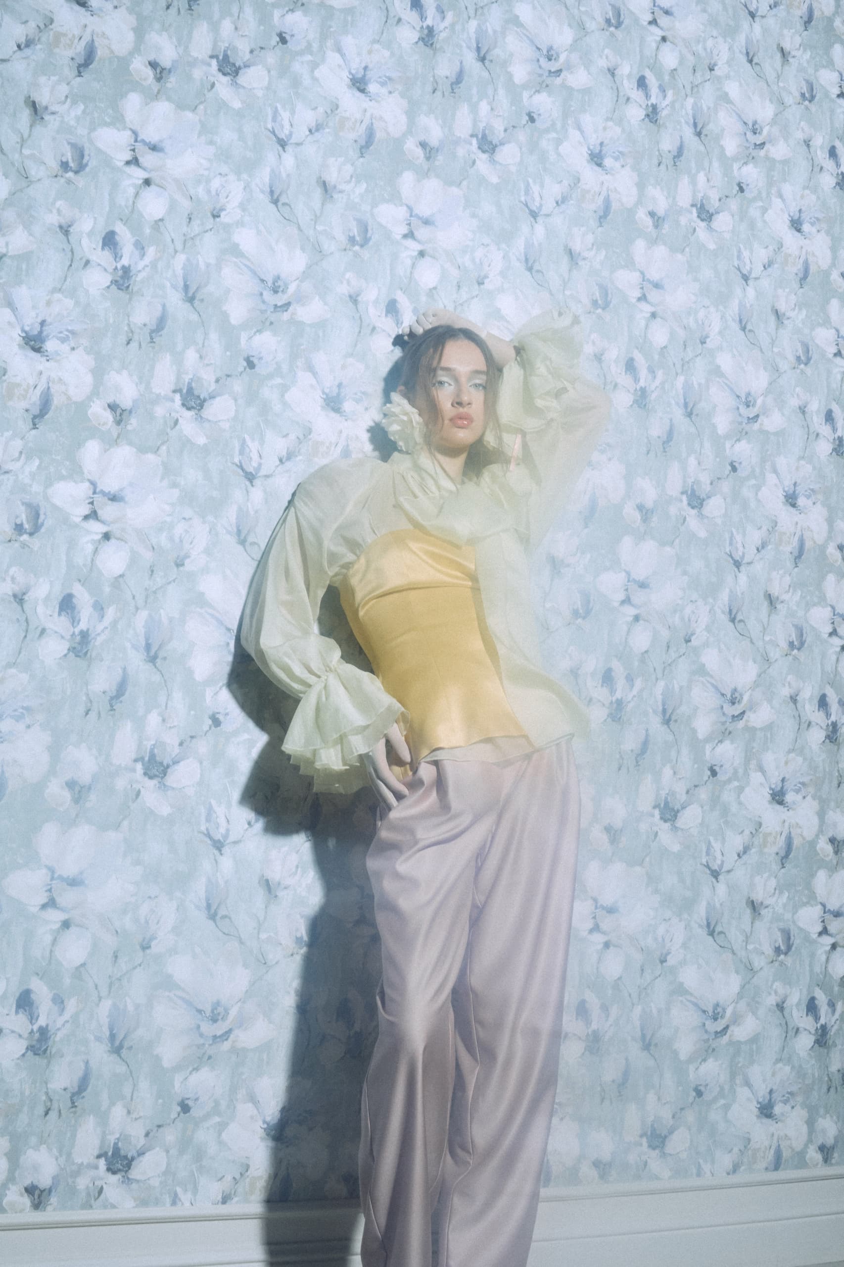 Fashion model in pastel outfit, floral wallpaper background.
