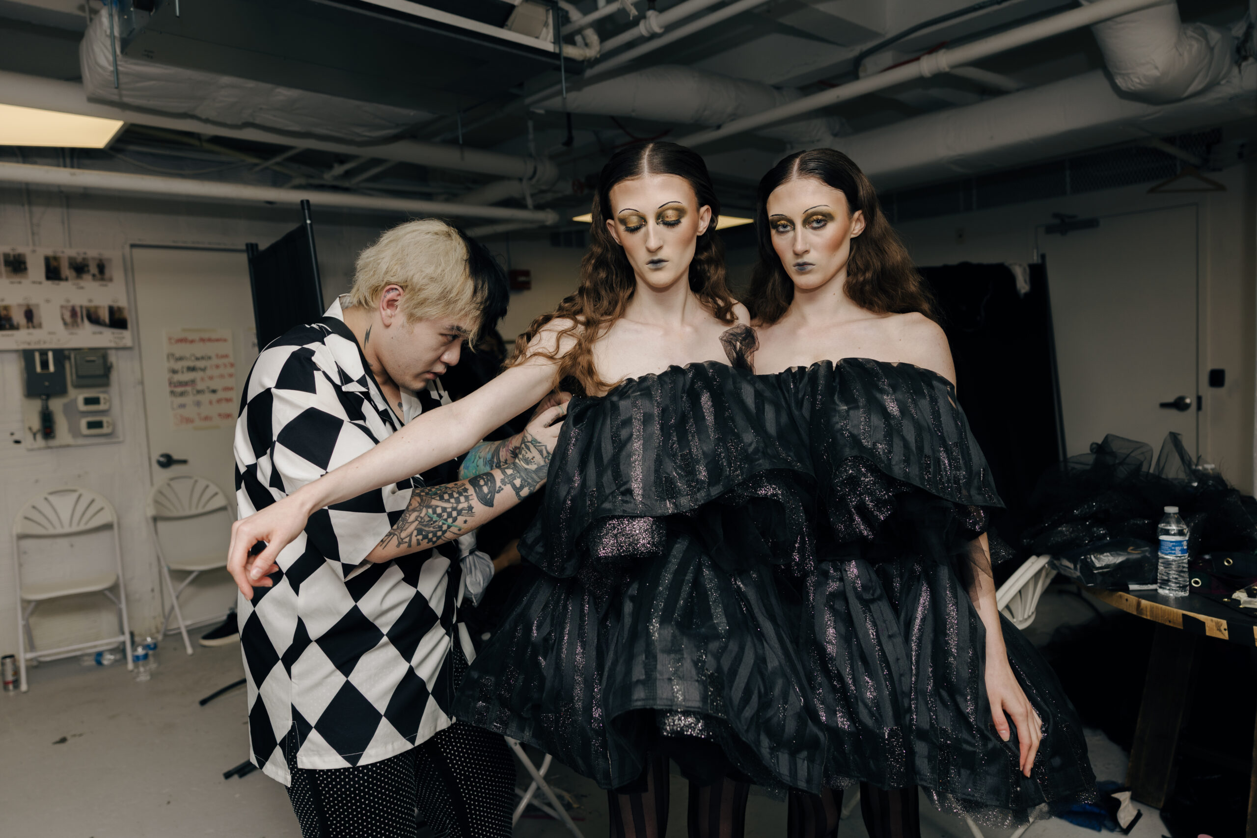 Designer adjusting dresses on models backstage runway show.