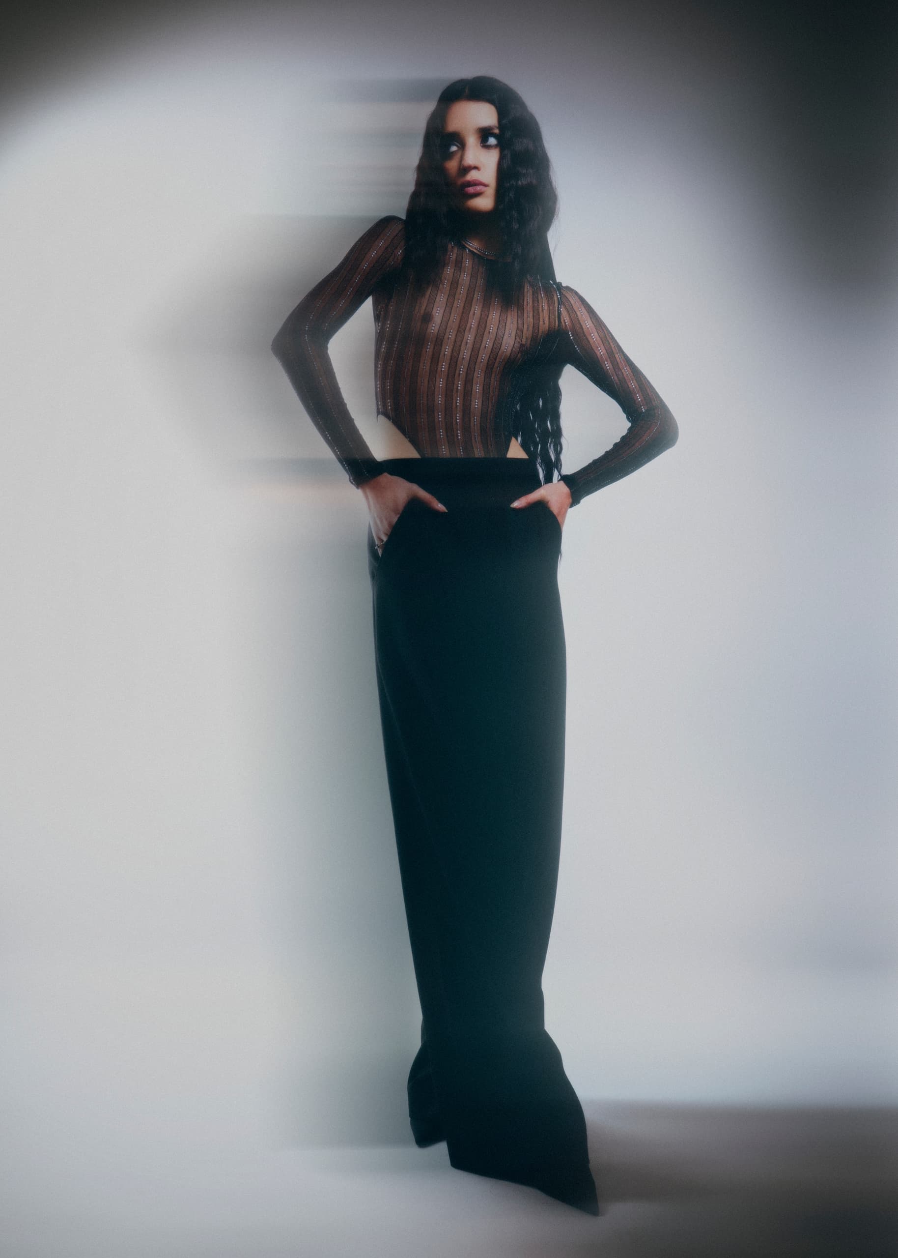 Stylish woman in sheer top and black skirt, with motion blur effect in studio lighting.