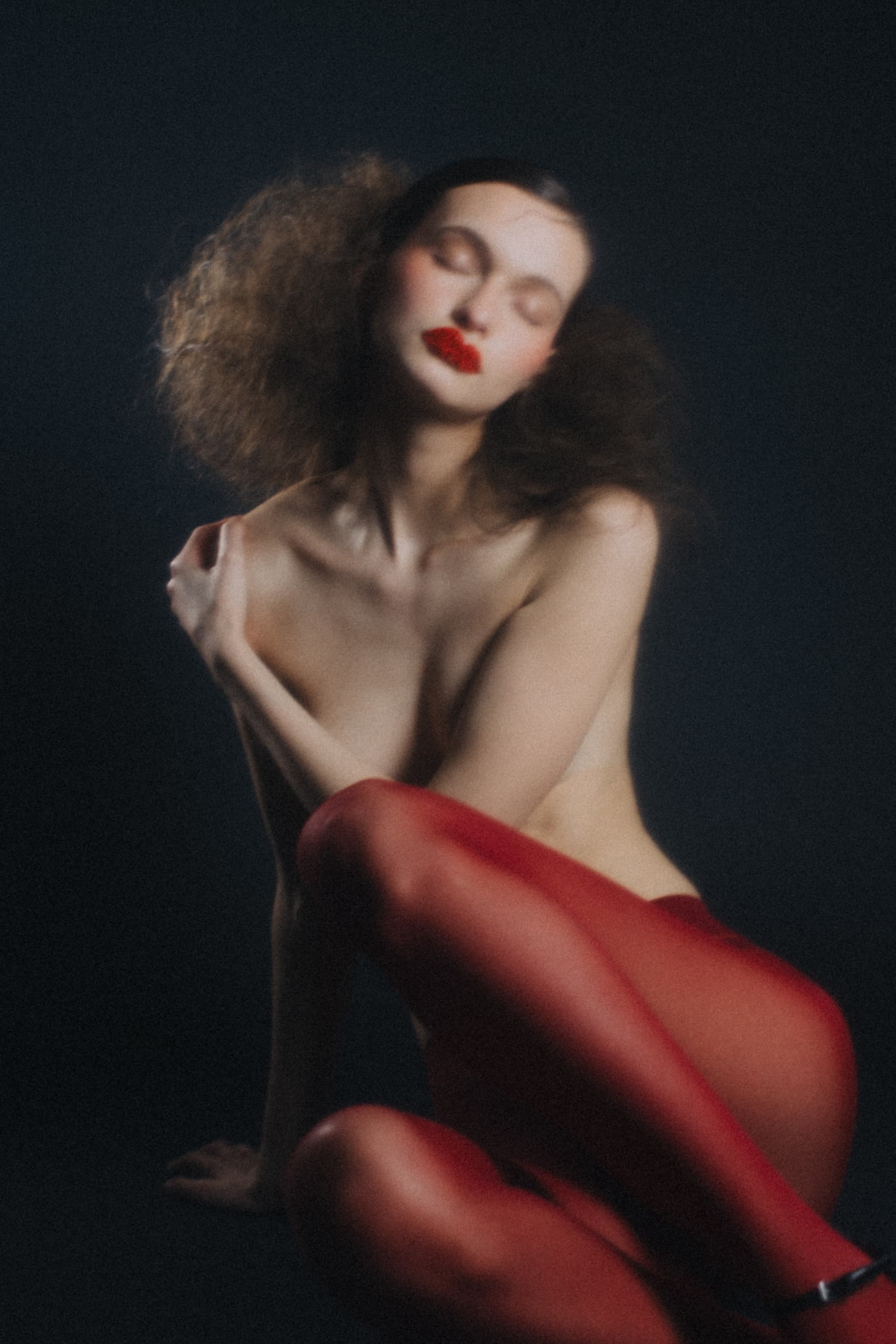 Artistic portrait of a woman in red tights with dramatic makeup on a dark background.
