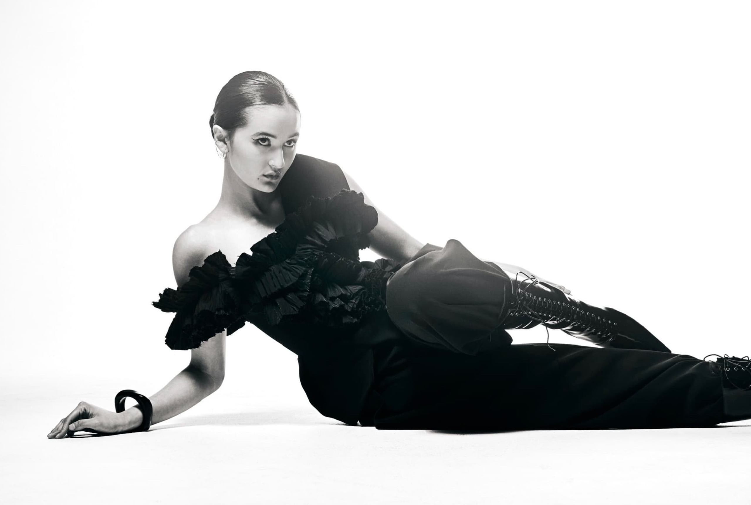 Fashion-forward woman in black dress posing elegantly on white background.