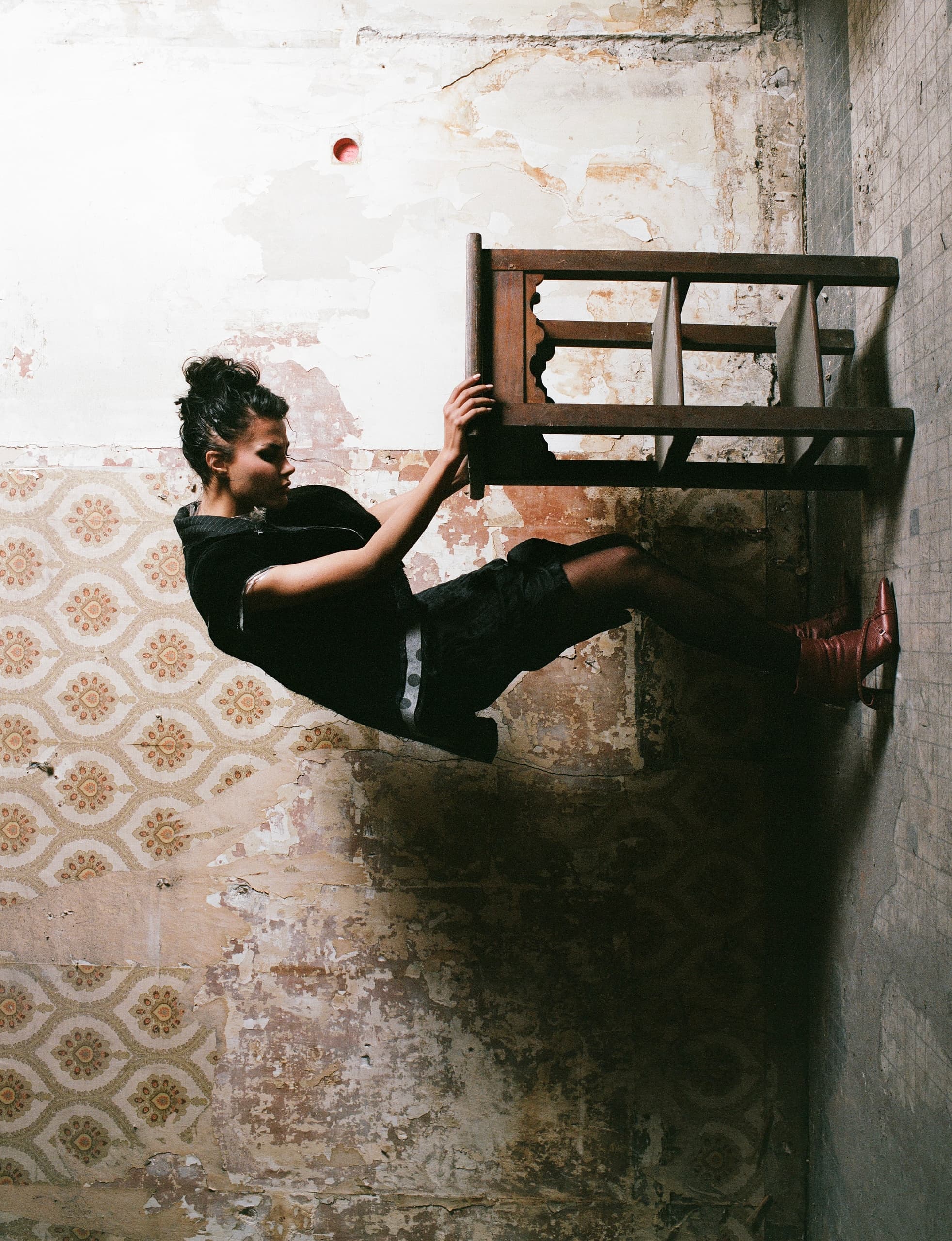Person balancing on chair against wall in vintage room.
