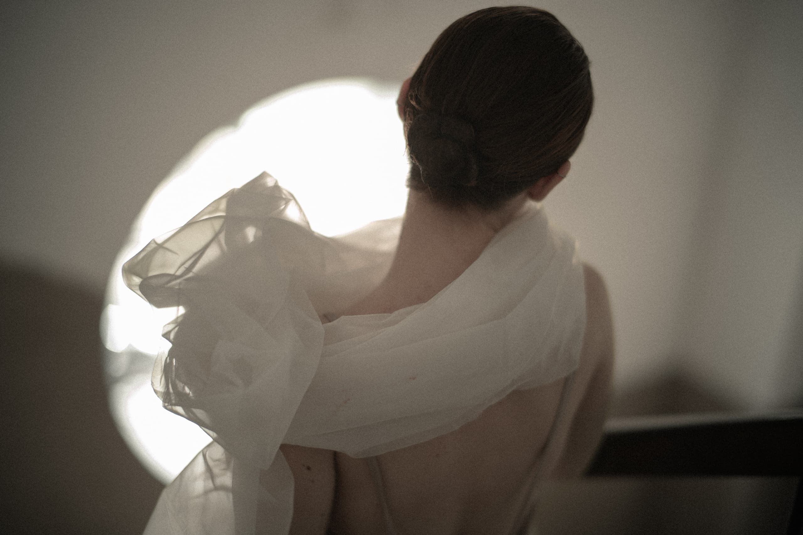Elegant woman in white gauzy dress with bun hairstyle, artistic back view.