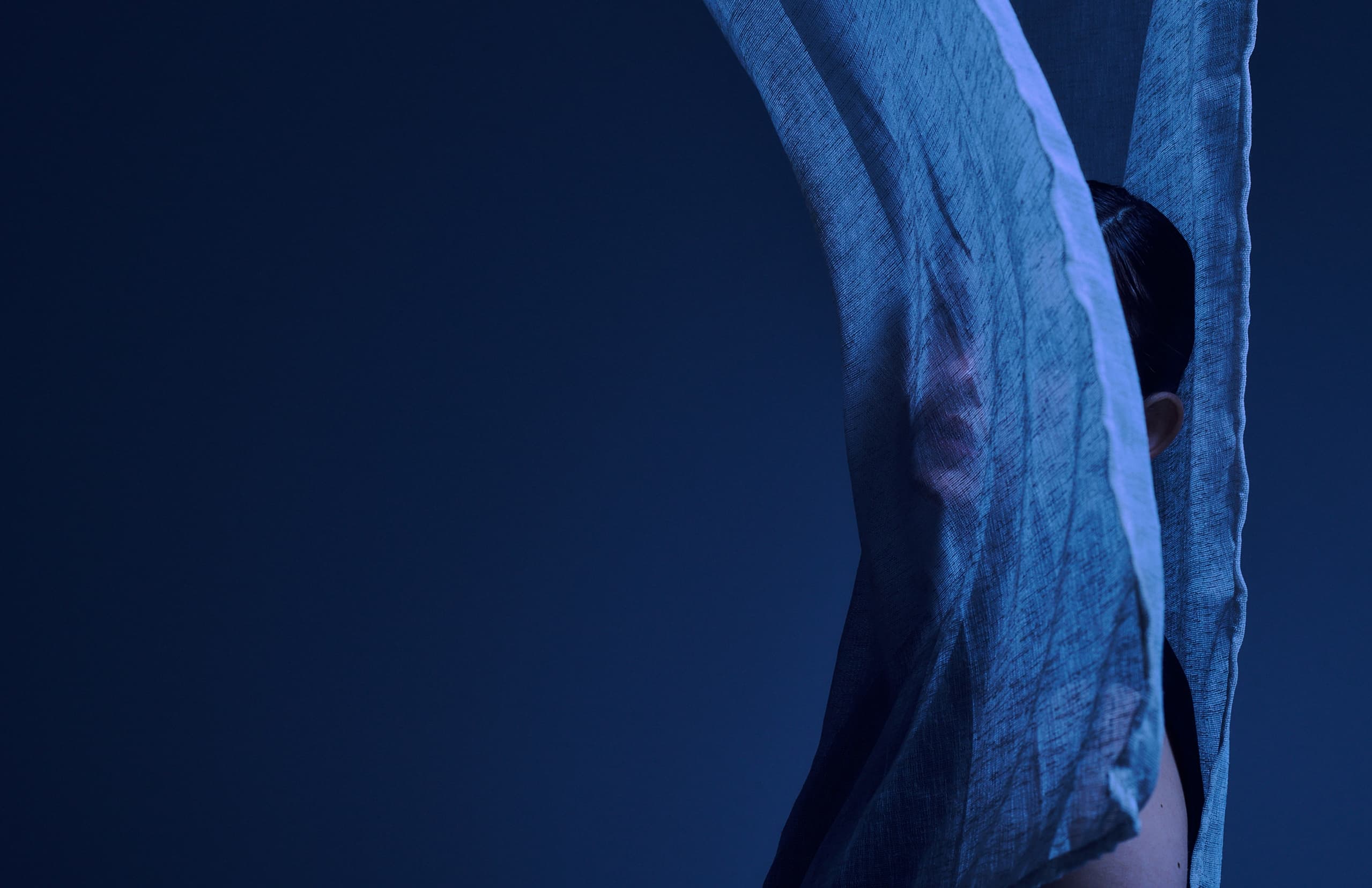 Mysterious figure behind sheer blue fabric in a dark, atmospheric setting.